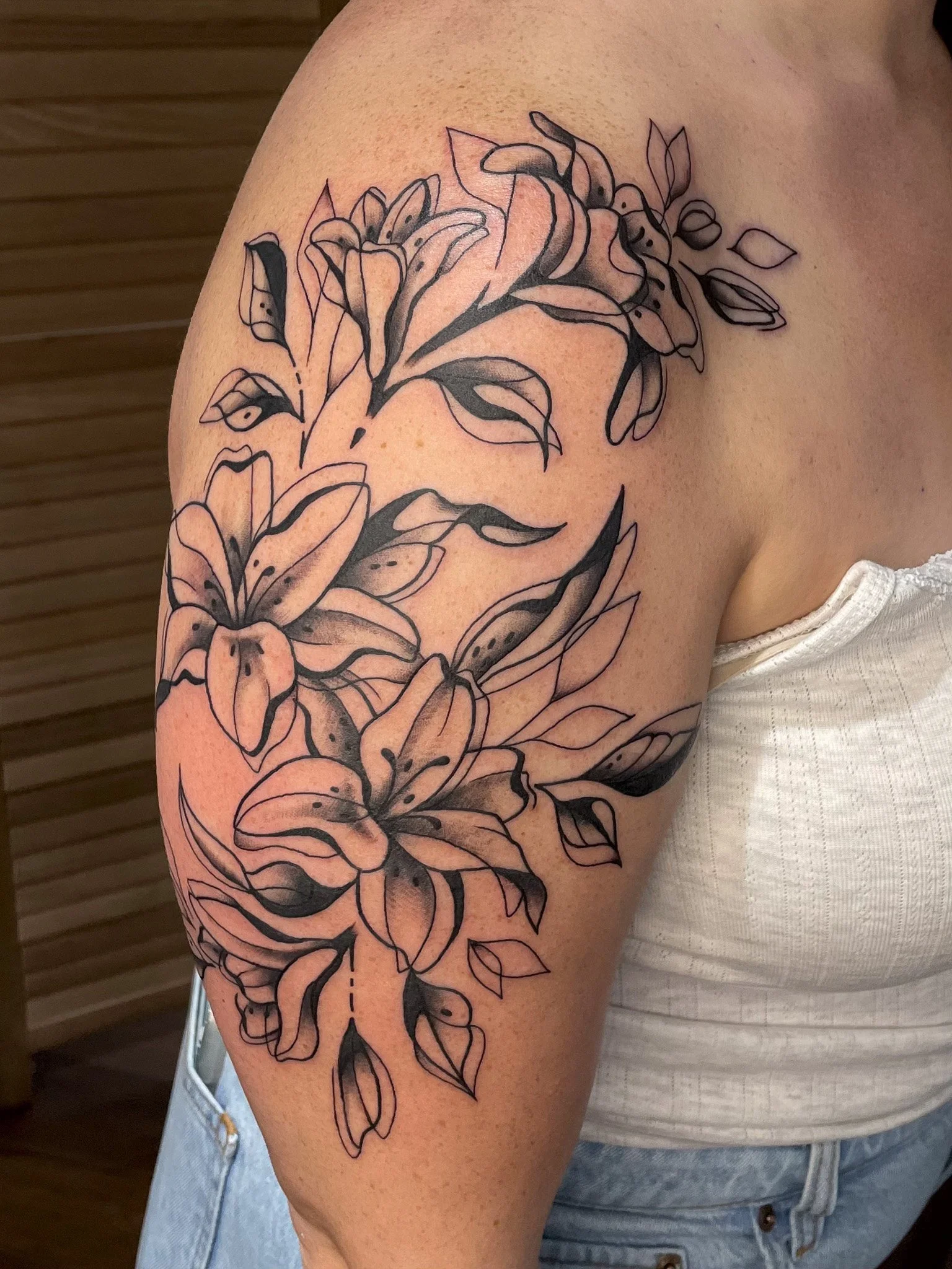 Black and gray floral tattoo on person's upper arm featuring lilies and leaves.