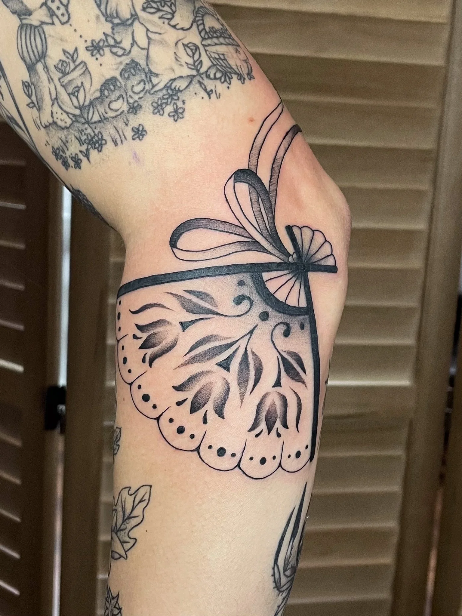 Black tattoo of a butterfly on a person's upper arm with floral and leaf patterns.