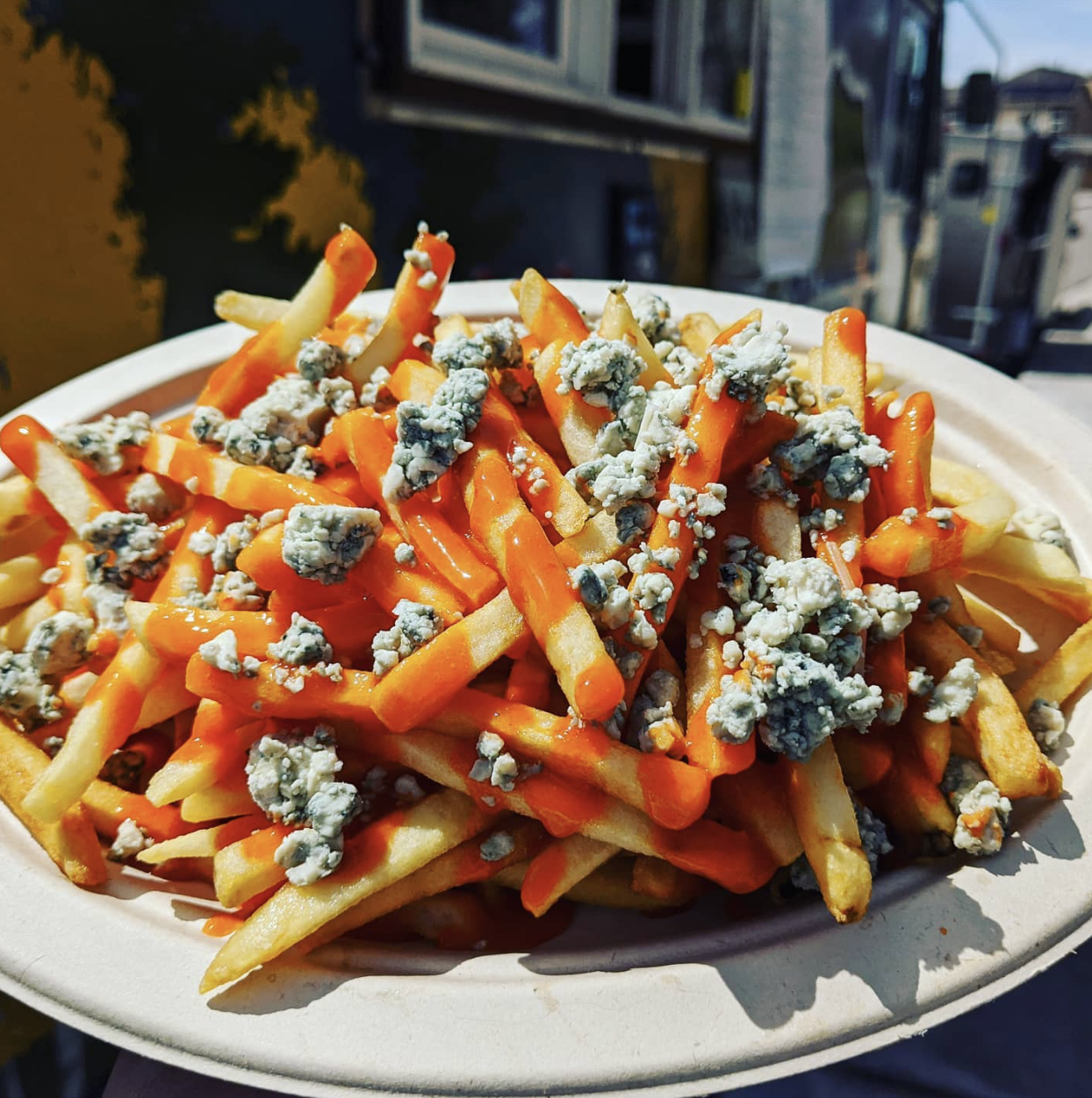 French fries topped with orange cheese sauce and blue cheese crumbles on a disposable plate.