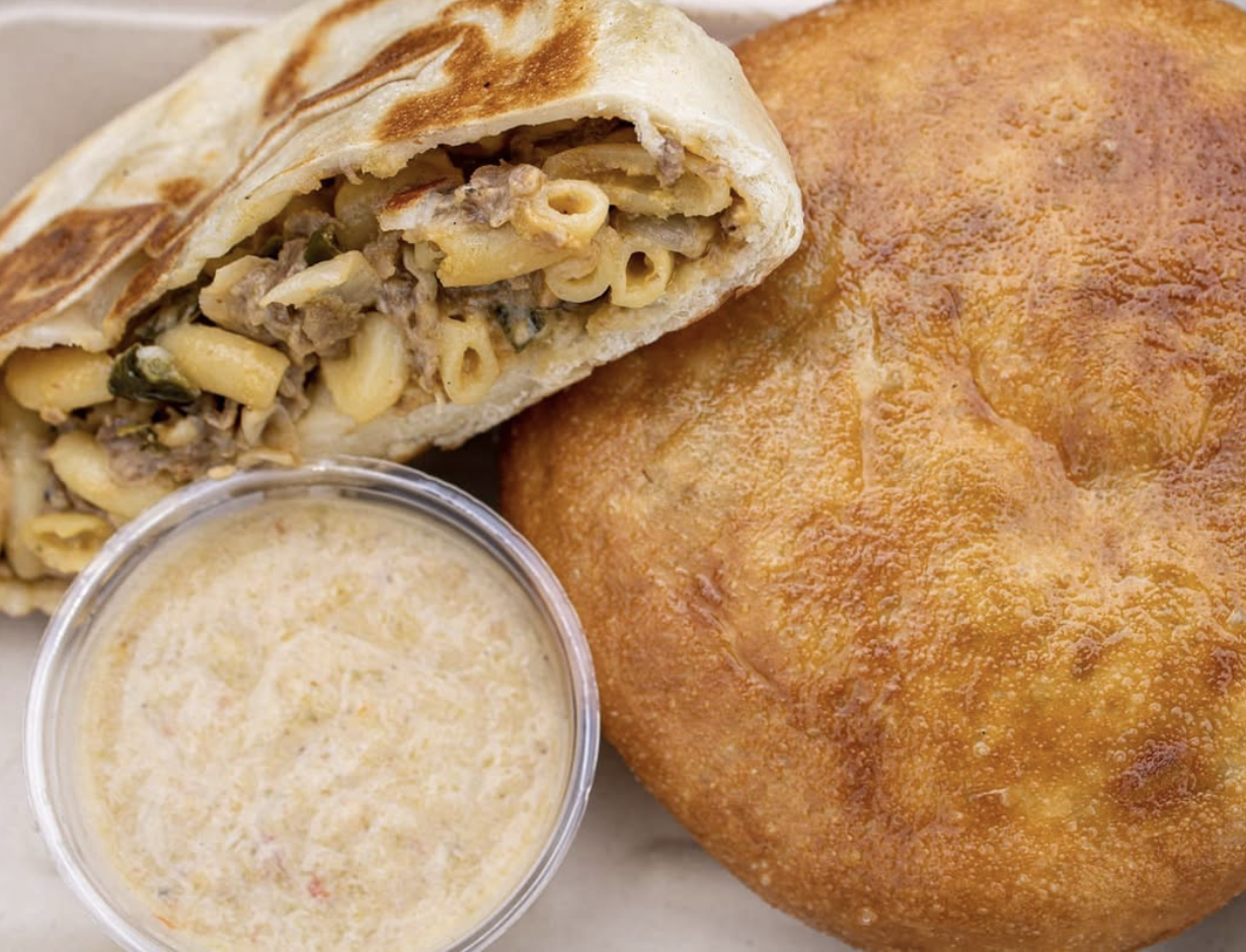 A calzone filled with pasta and beef, a container of ranch dressing, and a large golden fried ziti.