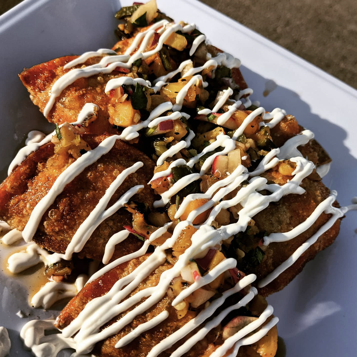 Close-up of three fried fish fillets topped with chopped vegetables, drizzled with white sauce, on a white plate.