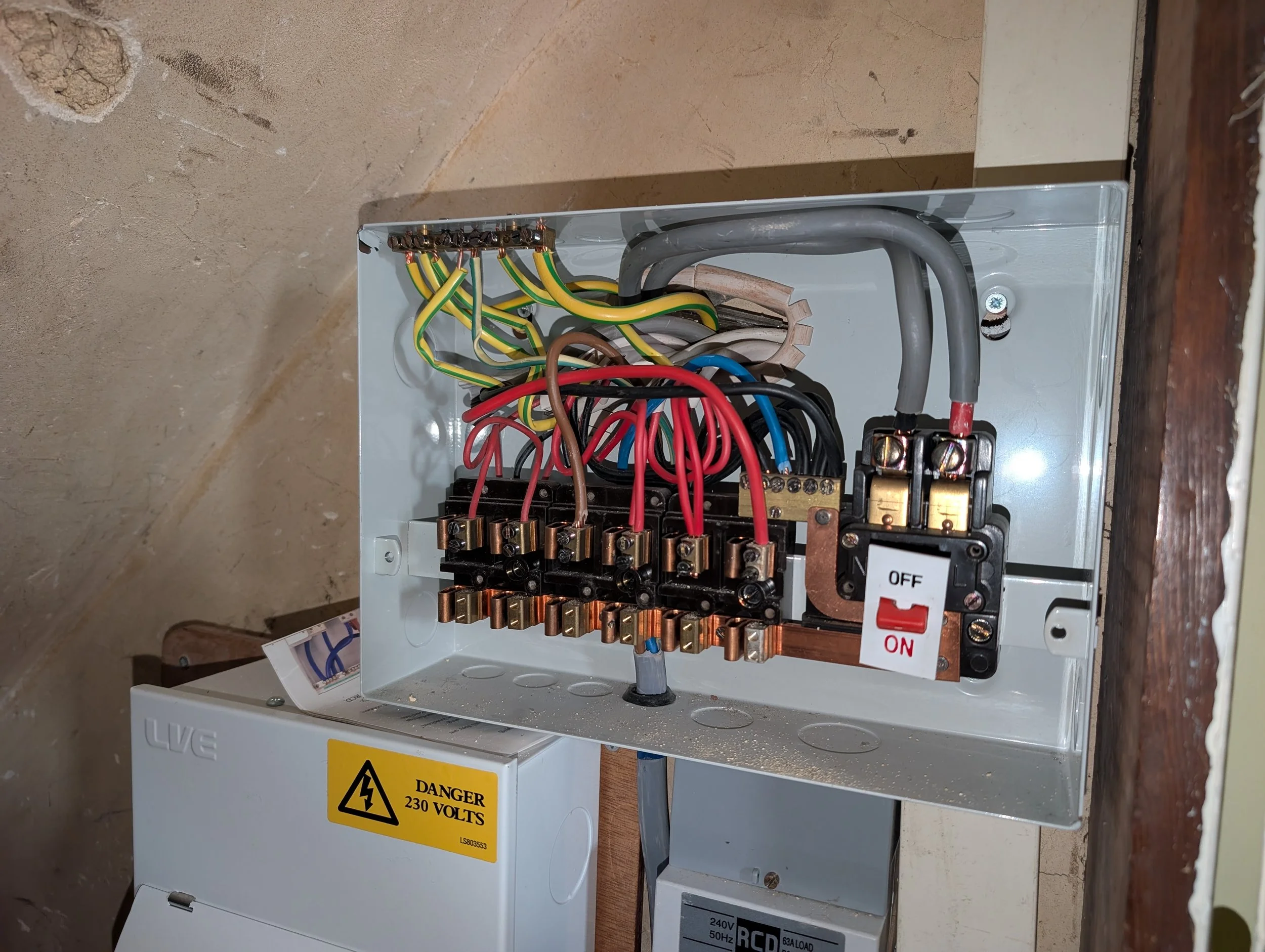 Open electrical circuit breaker box with multiple colored wires connected to switches and circuit breakers, next to a warning sign indicating danger of 230 volts.