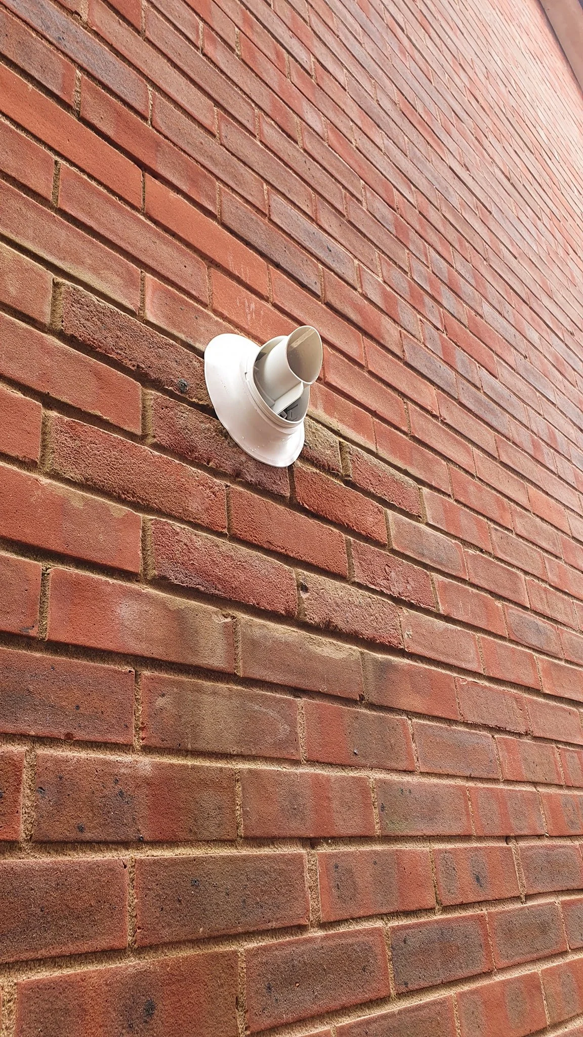 A white circular wall vent with a beige cover on a red brick wall.