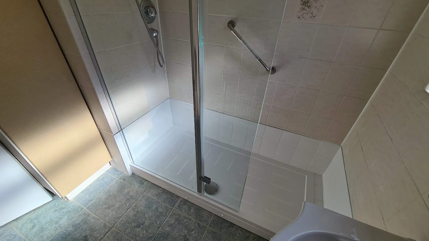 Shower with glass door, beige tiles, metal handrail, and white shower base in a bathroom.