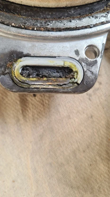 Close-up of a small engine part with visible carbon buildup and dirt around an exhaust port.