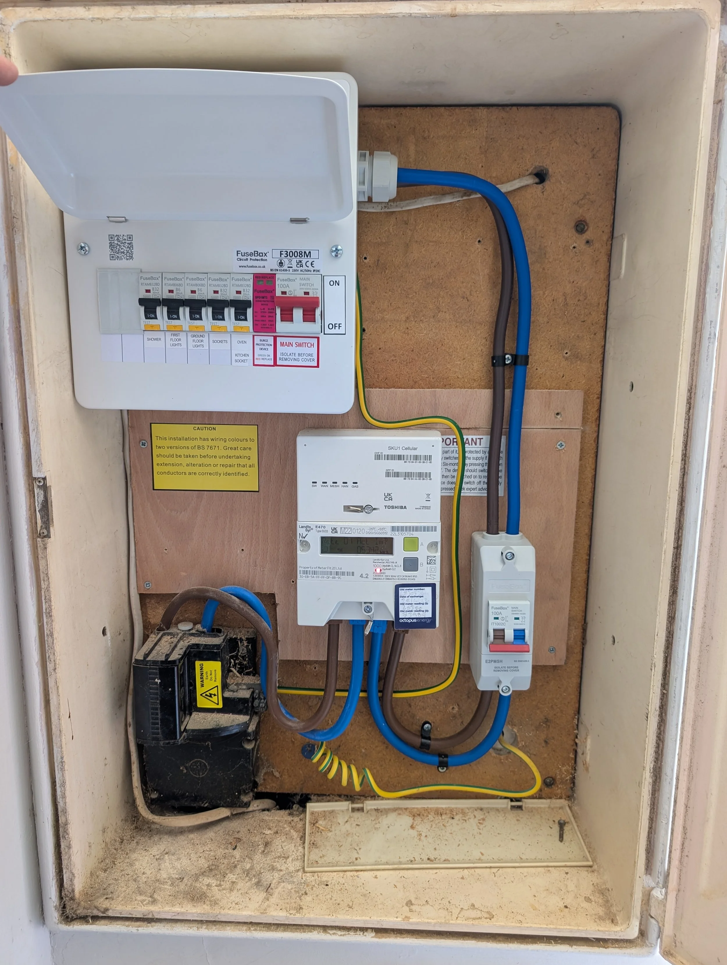 Electrical panel with multiple circuit breakers, connections, and a digital energy meter inside a box, mounted on a wall in a utility space.