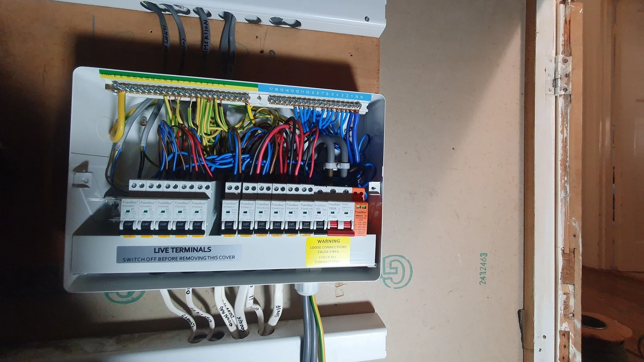 Electrical breaker box with multiple colored wires and circuit breakers inside a box on a wall.