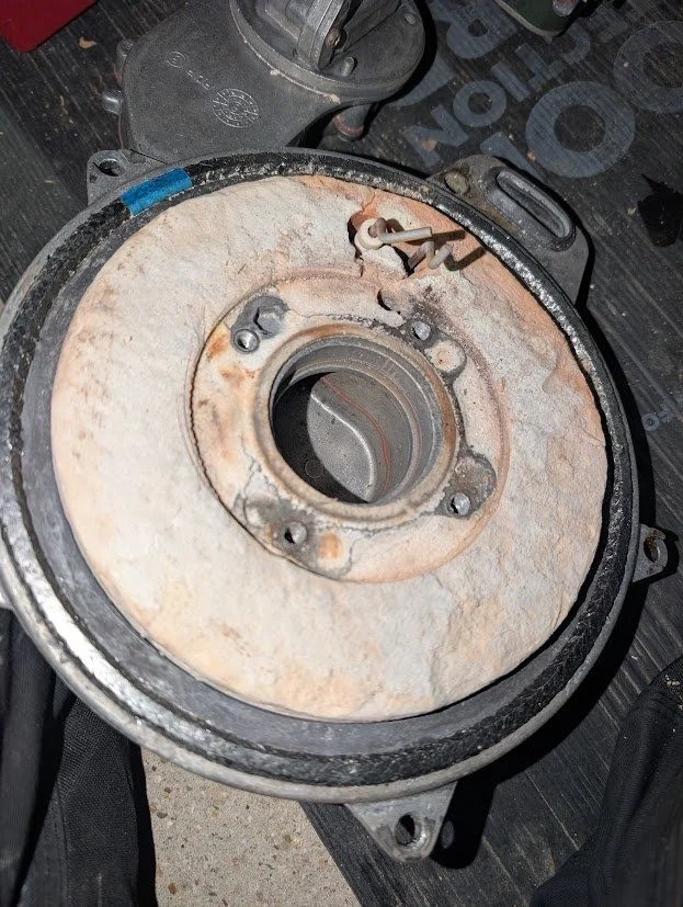 Close-up of a rusty mechanical part, likely a motorcycle or vehicle engine component, with a central opening and bolts around it, resting on a work surface.