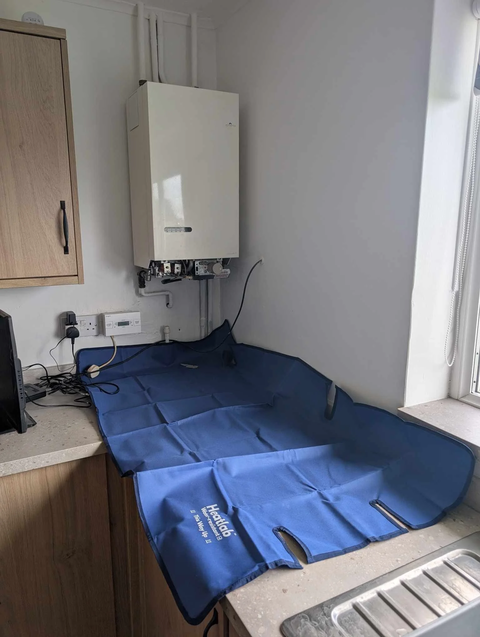 A blue heated underbody pad on a kitchen countertop with a boiler mounted on the wall above it.