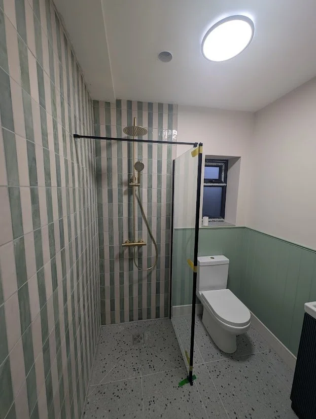 Bathroom with a walk-in shower, toilet, and window, separated by a glass partition.