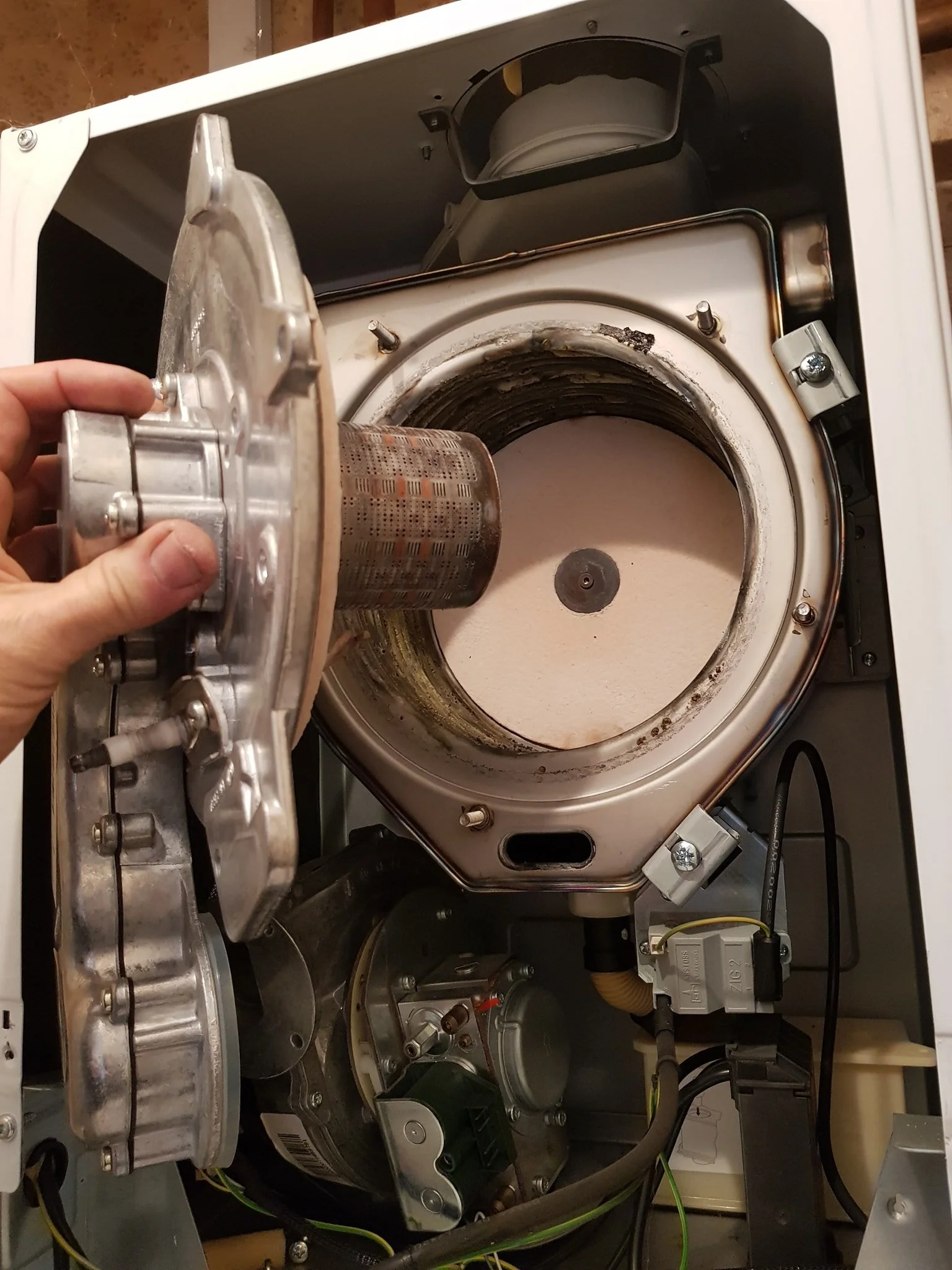 The inside of a washing machine with its top removed, showing the drum and motor assembly, and a hand holding a metal part.