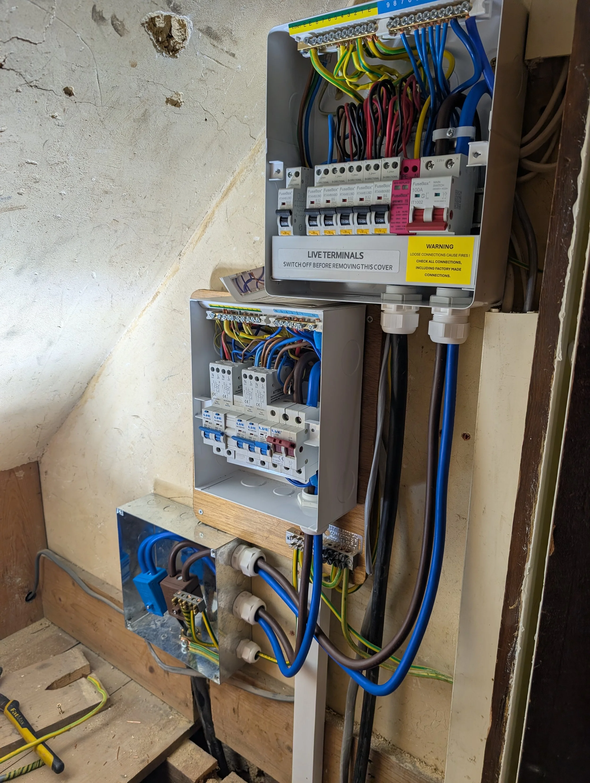 Electrical panel with multiple circuit breakers and wiring, mounted inside a wall. Wires are connected to various components, with some labeled and color-coded.