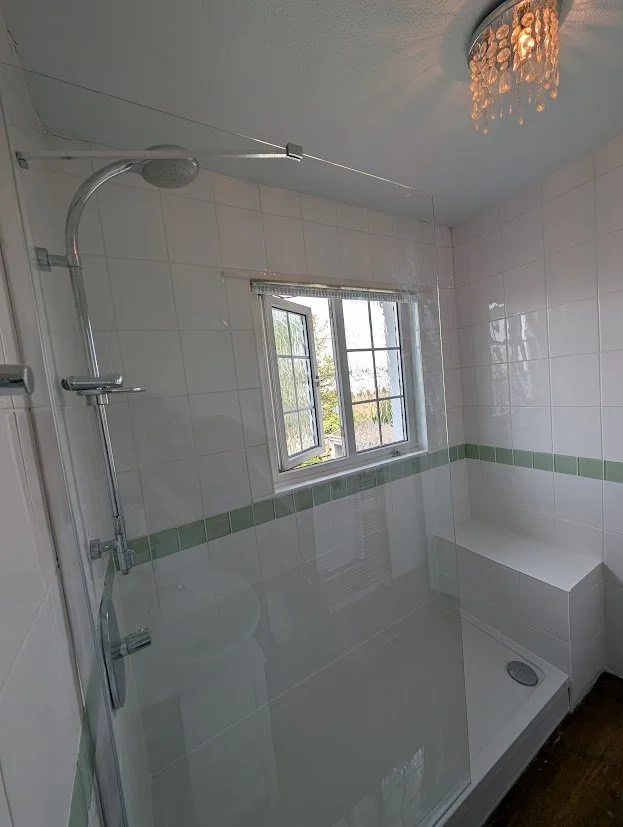 Empty bathroom corner with a shower area, small window, tiled walls, and a ceiling light fixture.