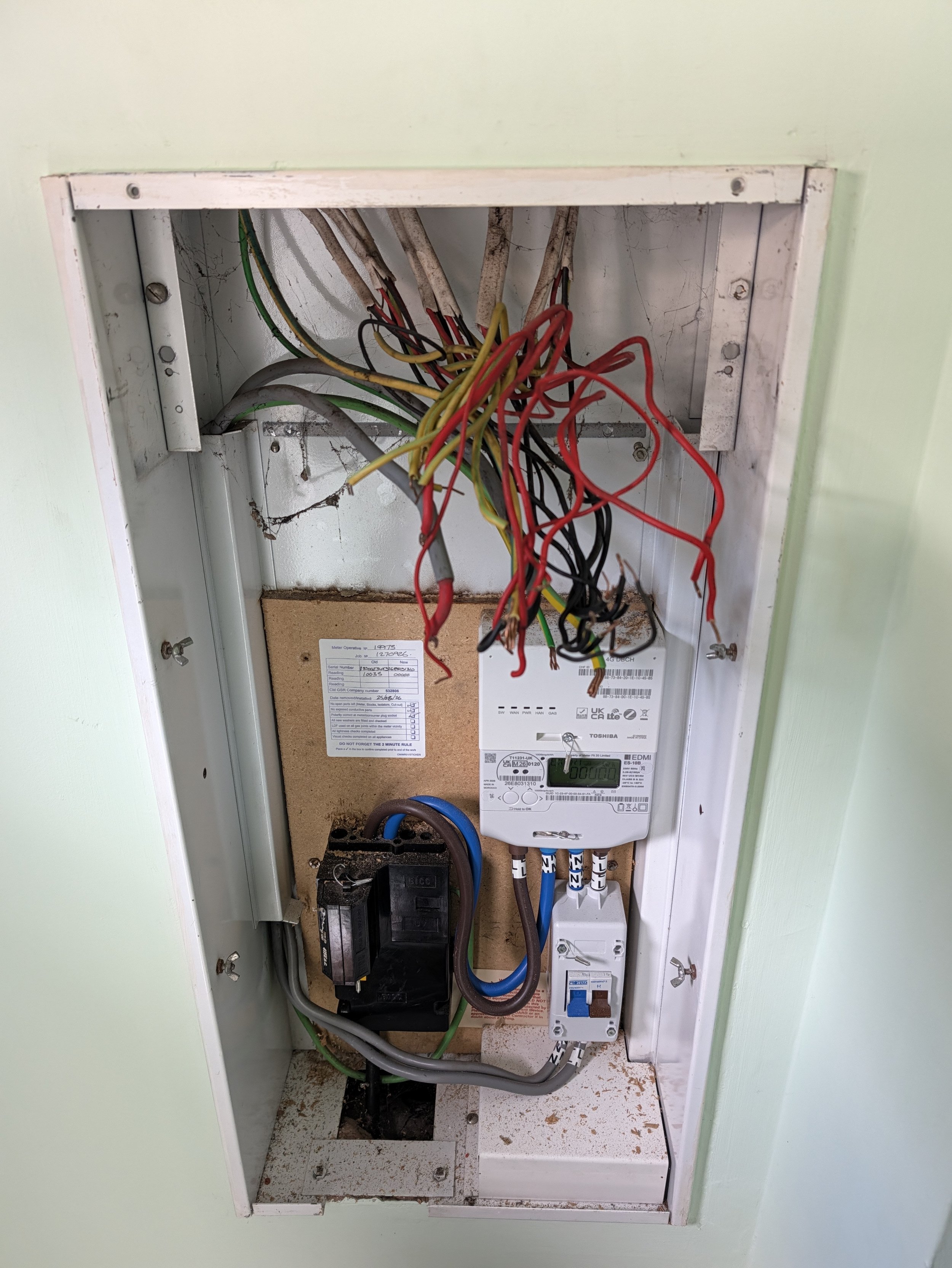 Electrical wiring box with tangled wires, disconnect switch, and circuit meter inside a wall cavity.