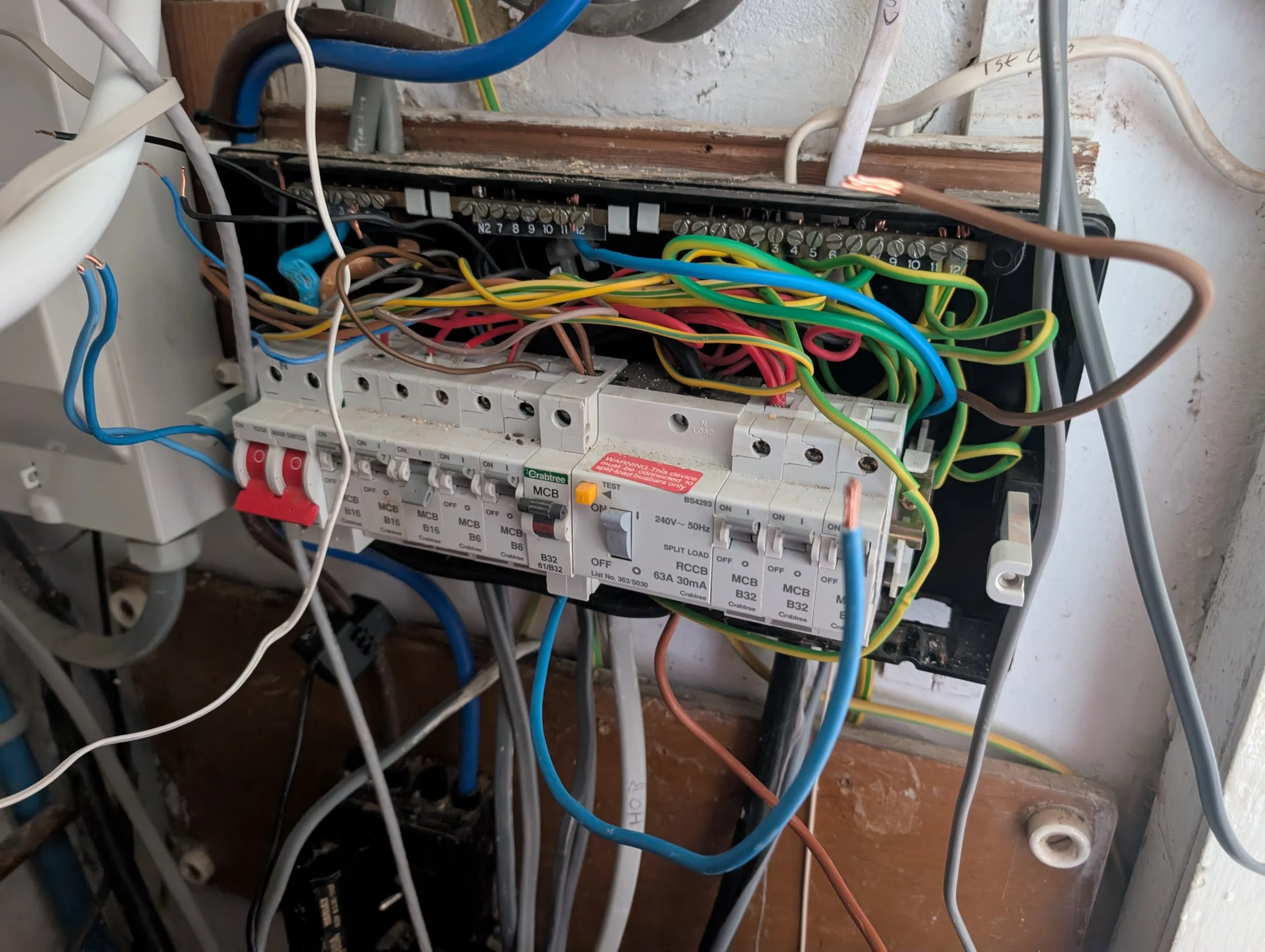 Open electrical breaker panel with multiple colored wires and circuit breakers inside.