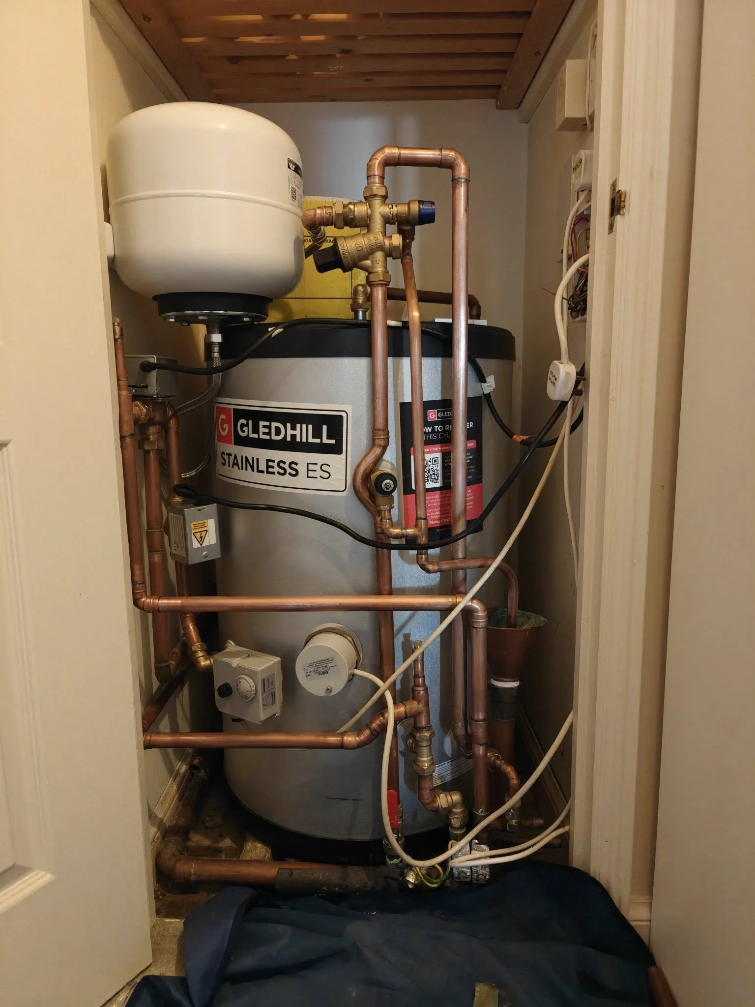 A water heater system with copper pipes and an expansion tank installed in a small utility closet.