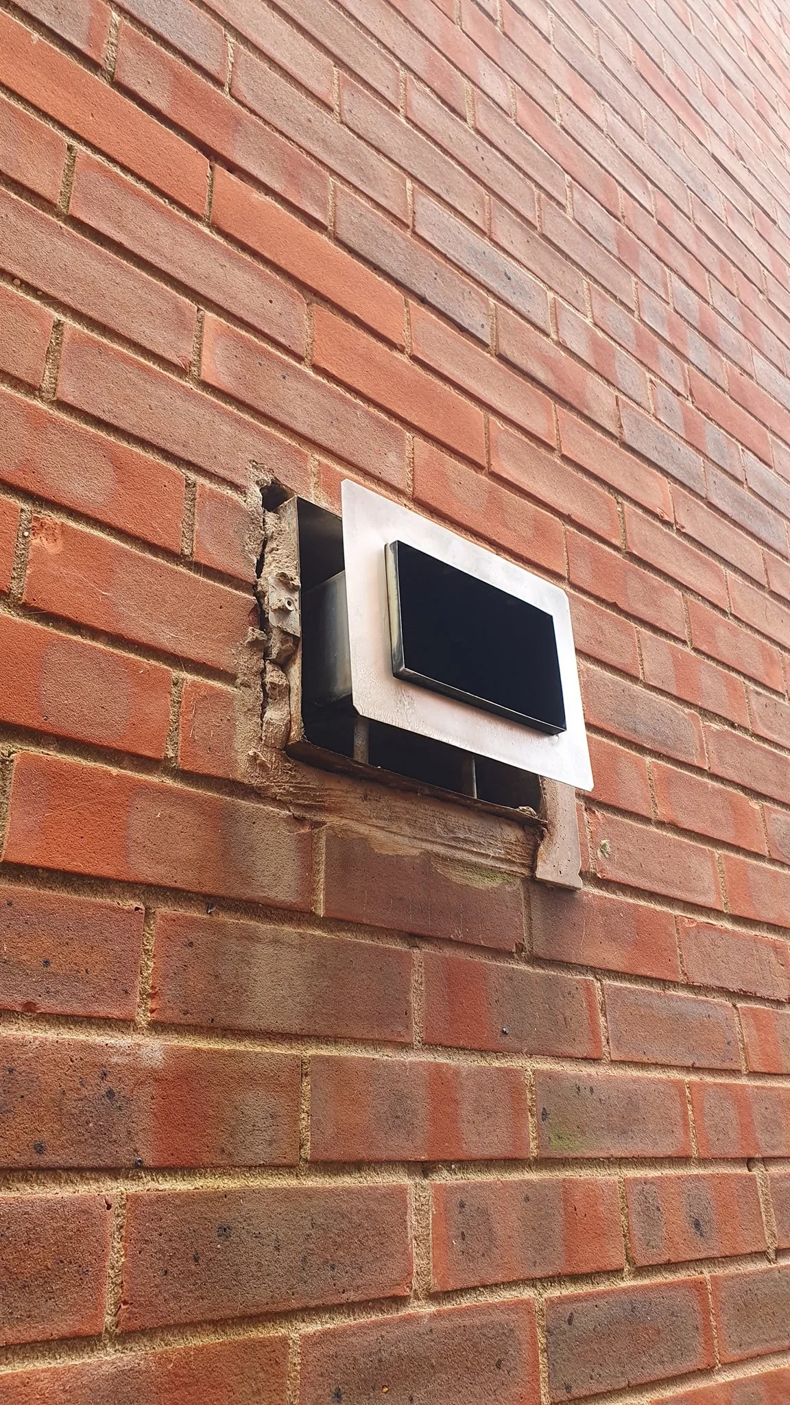 Close-up of a brick wall with a mounted electronic device or panel, partially installed with visible screws and a black area on the device.