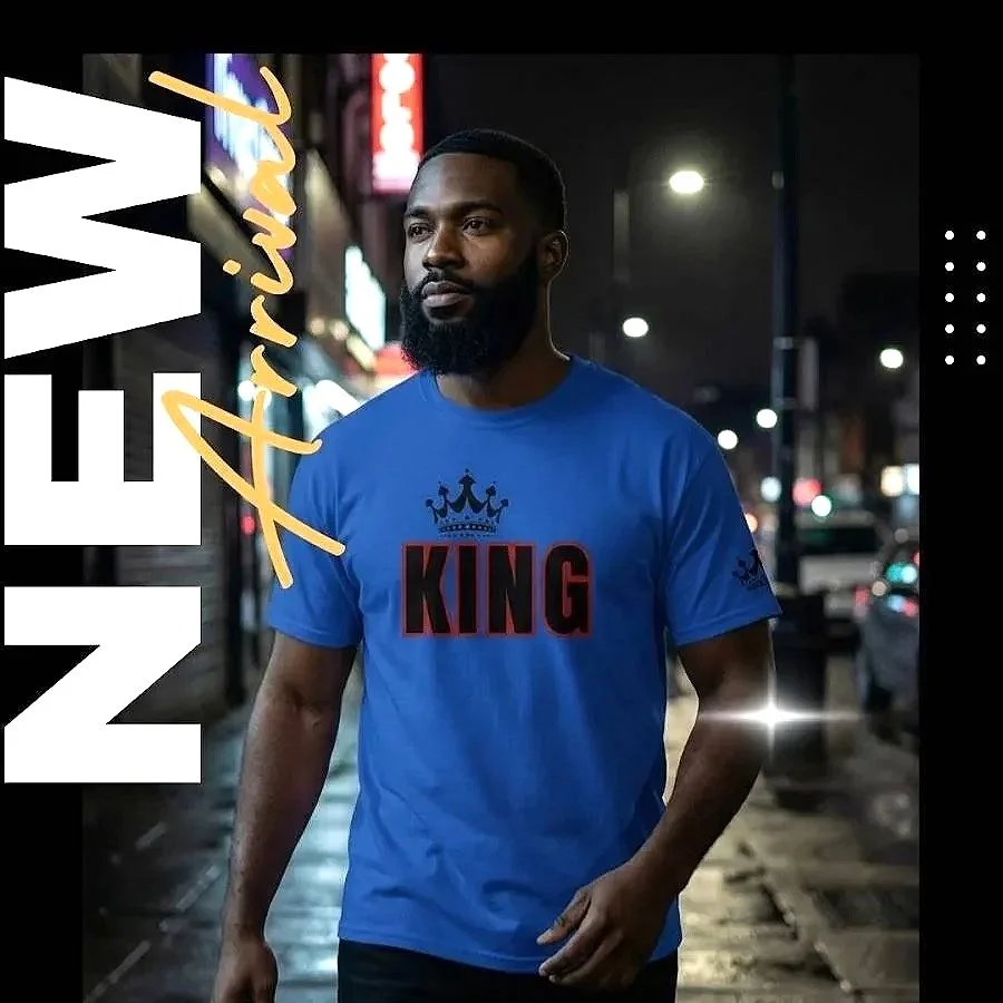 A man with a beard wearing a blue T-shirt with the words "KING" and a crown graphic walking on a city street at night with lights and signs in the background.