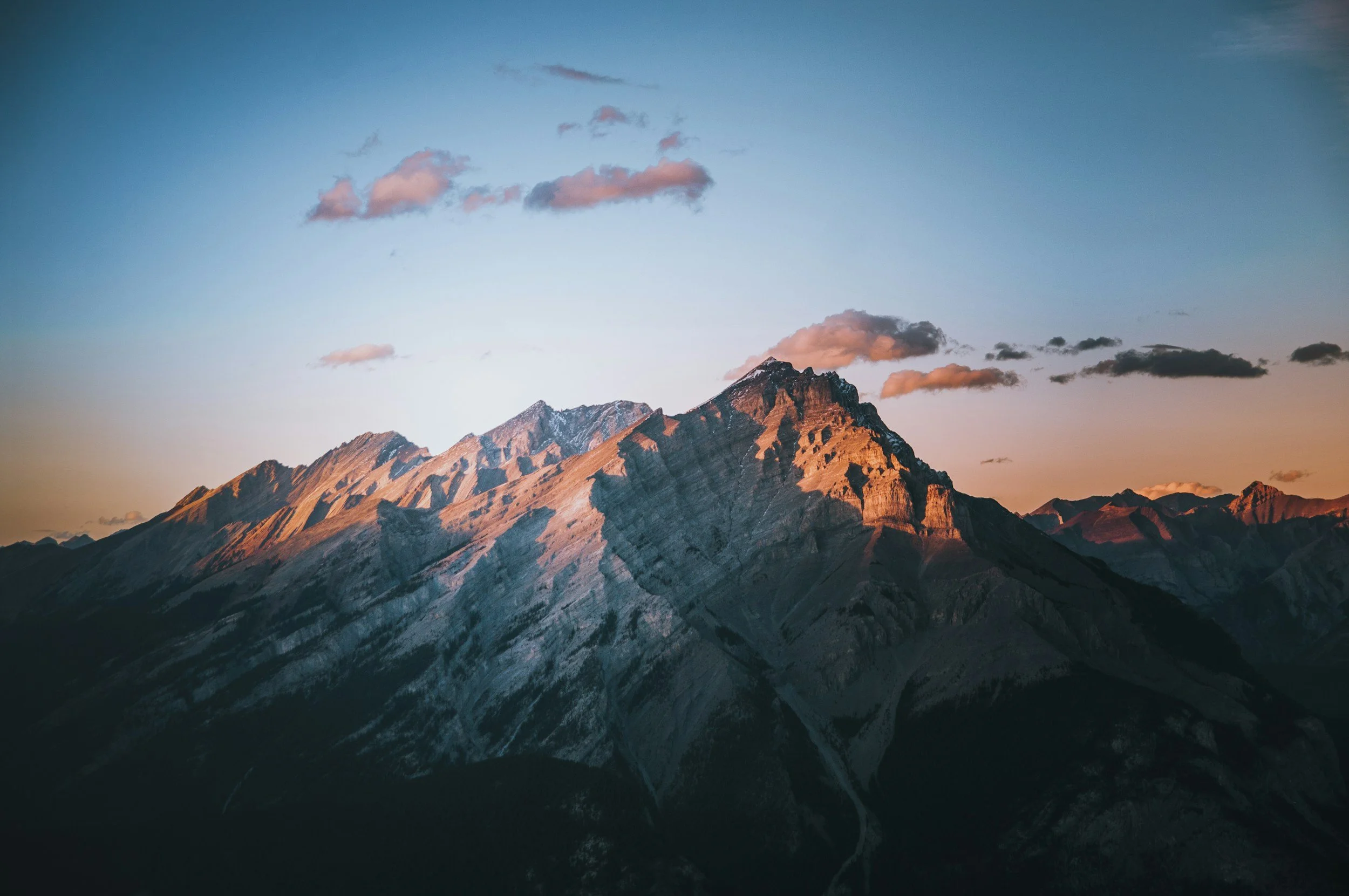 Sunset over rugged canadian mountain peaks with sparse clouds in the sky.