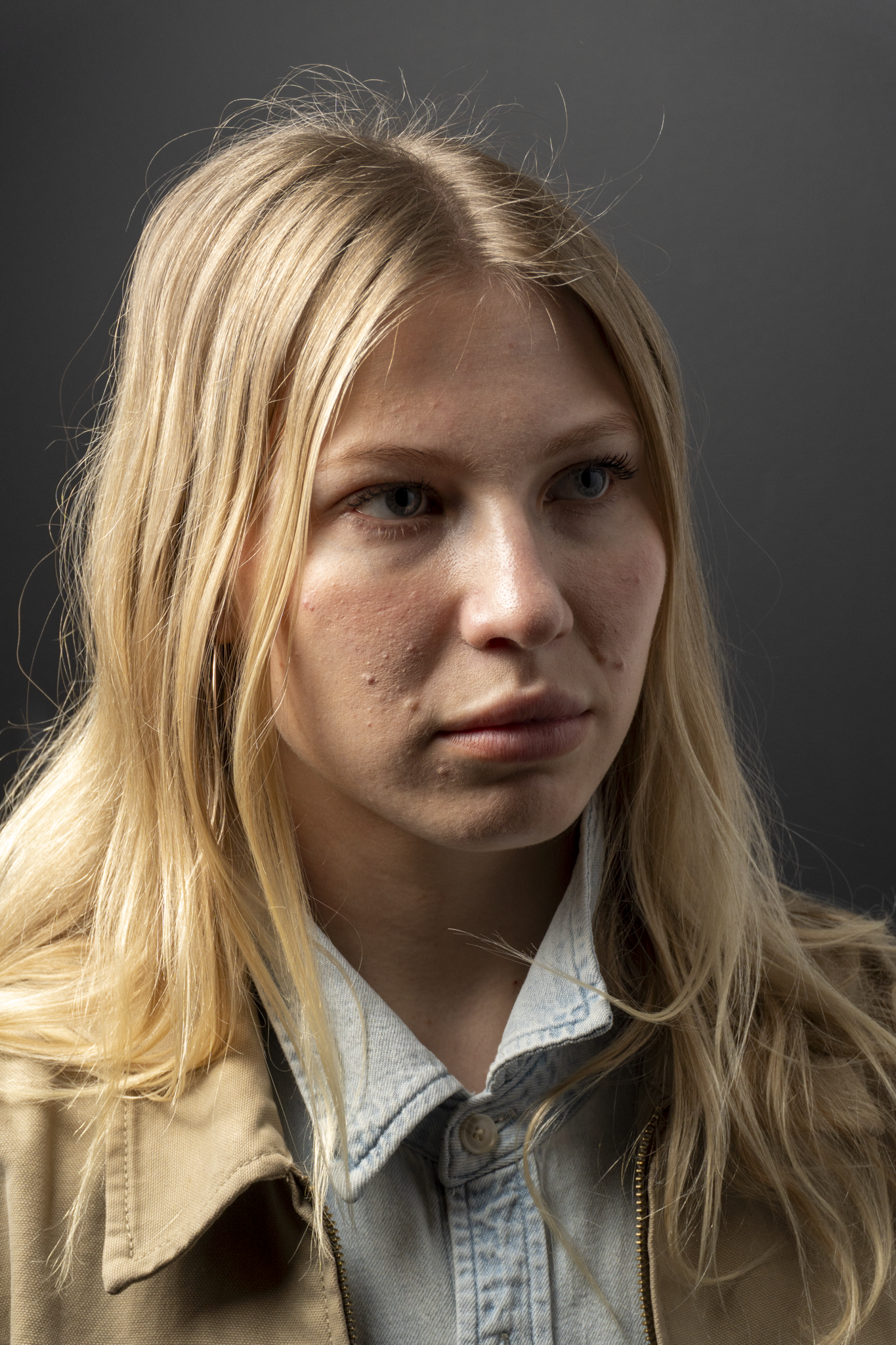Close-up portrait of a young woman with blonde hair and blue eyes against a dark background.