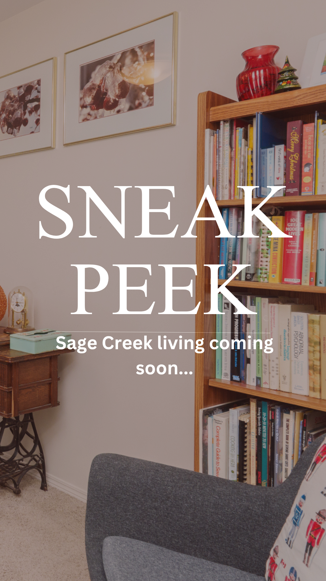 An interior room with a wooden bookshelf filled with books, a small side table with a green box and a vintage clock, a framed picture on the wall, and a gray chair. Overlaid text reads "Sneak Peek - Sage Creek living coming soon..."
