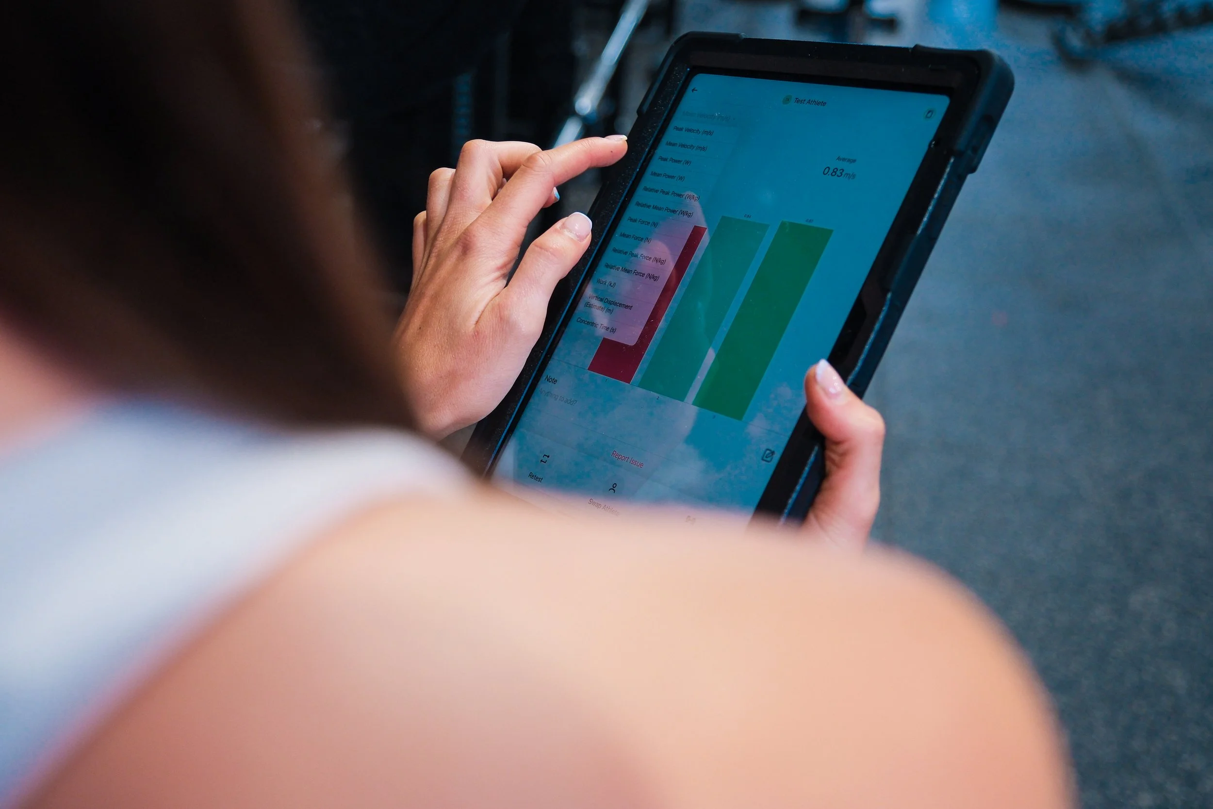 Person using a tablet to view performance metrics and bar graphs related to athlete testing, with a focus on sprint speed and force measures.
