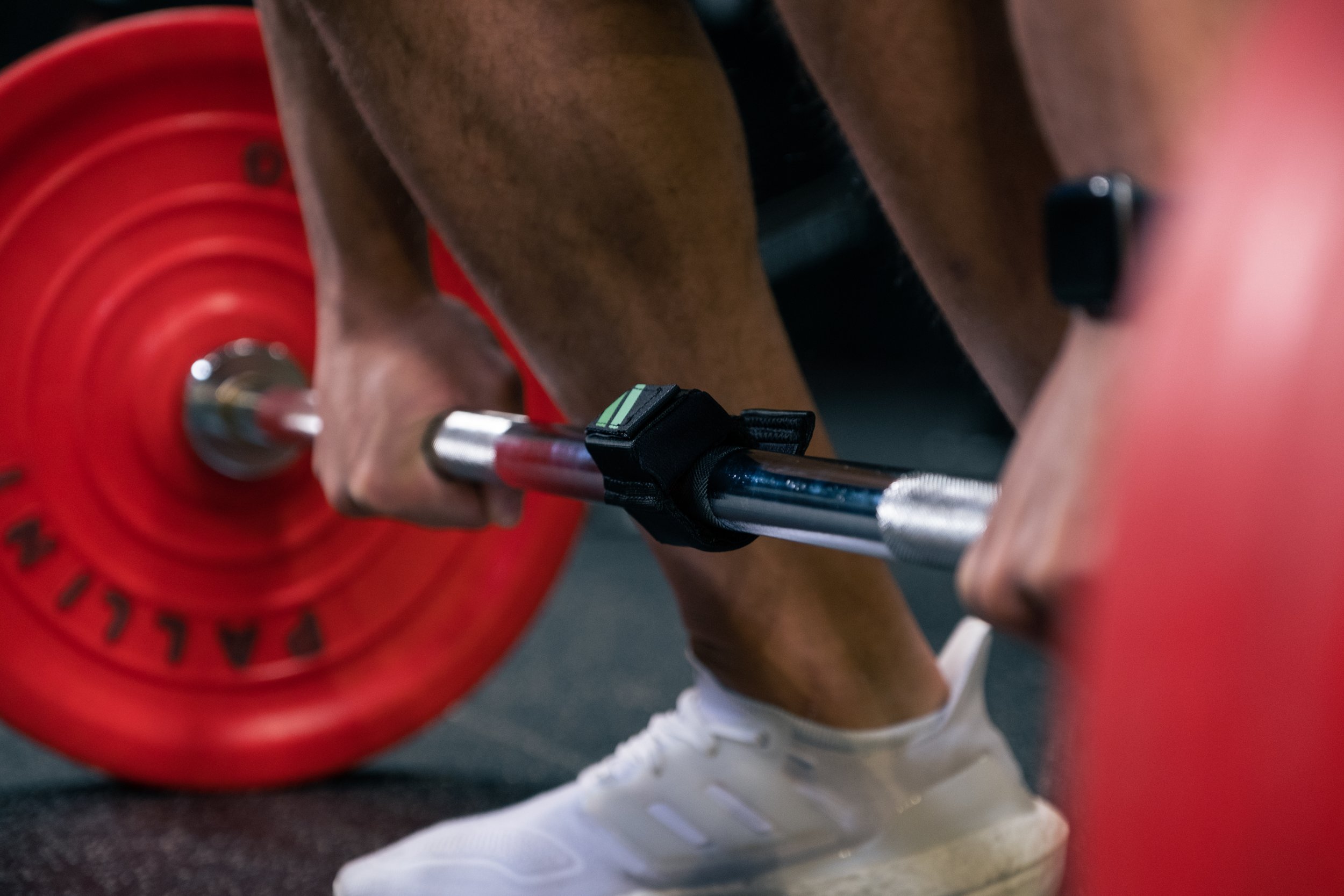 A person lifting a barbell with red weights during weightlifting, wearing white sneakers and a black wrist strap.