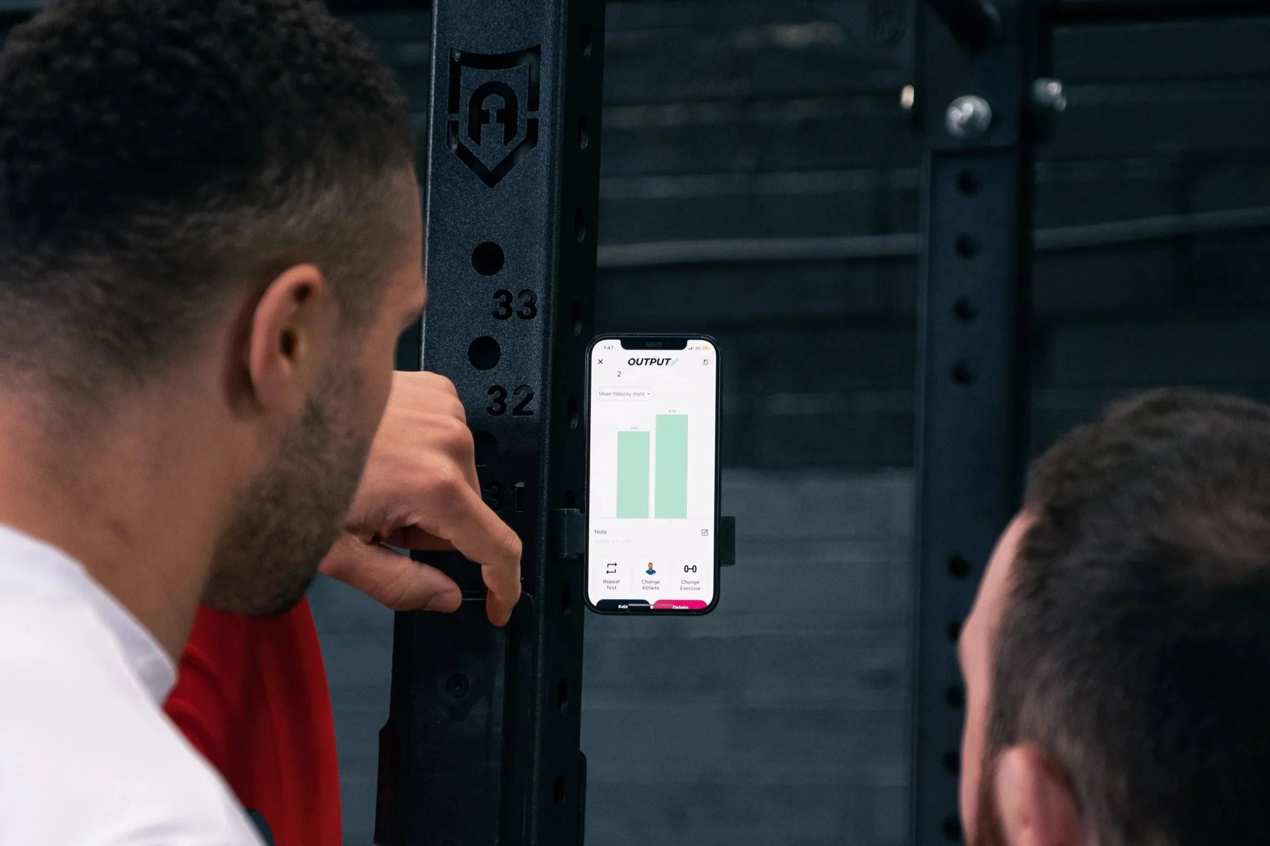 Group of people looking at a phone displaying a graph during a workout or sports activity in a gym.