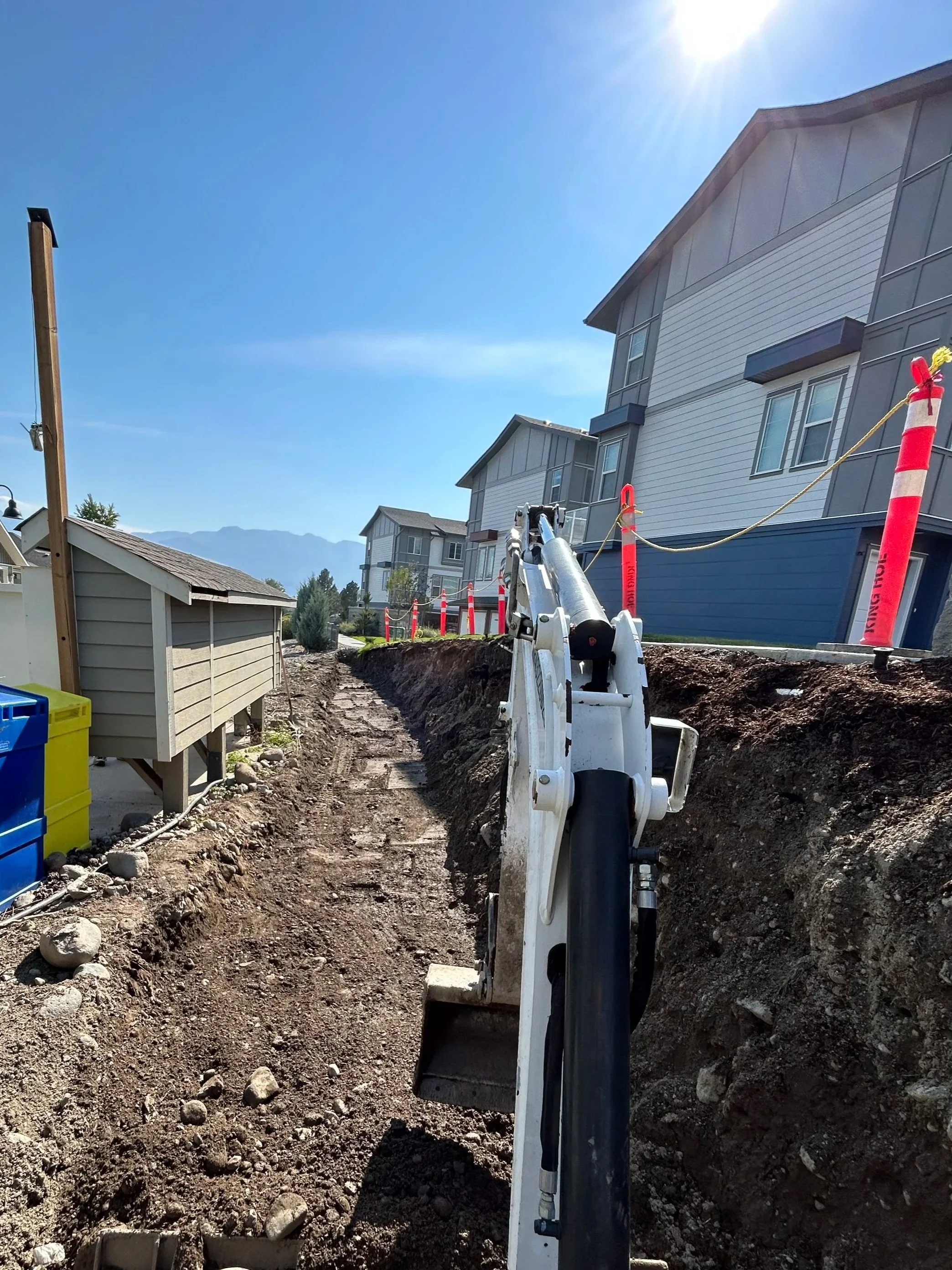 Construction site with an excavator digging a trench along a residential area, preparing to add a allen block wall