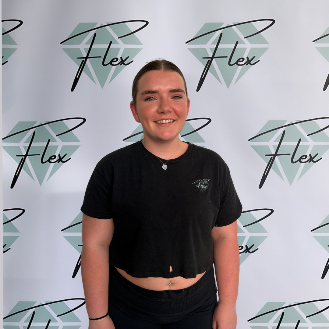 A young woman with dark hair in a bun, smiling in front of a step and repeat backdrop with the logo 'Flex' and a diamond graphic.