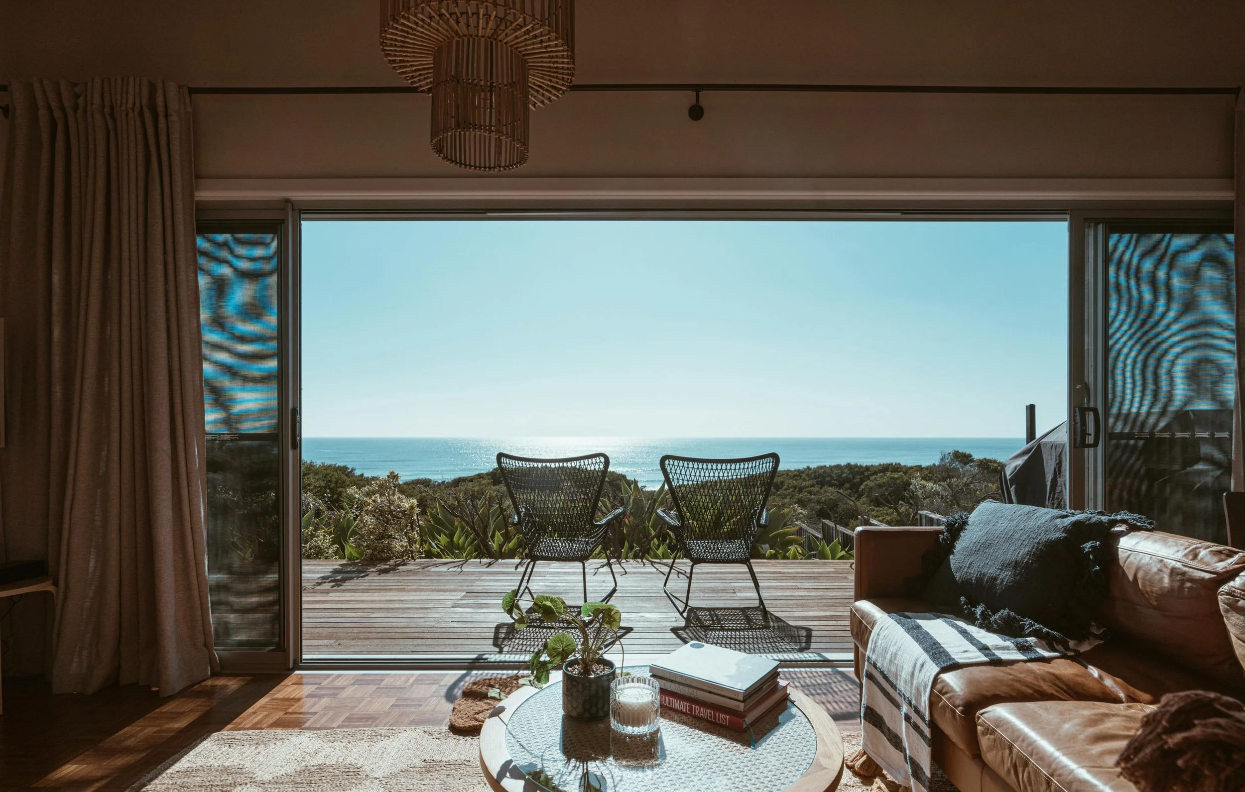Living room opening to deck with two black chairs and ocean view