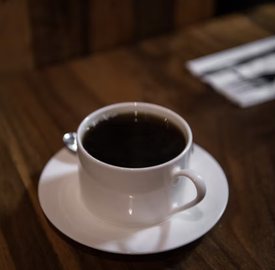 White coffee cup filled with black coffee on a matching saucer, placed on a wooden table.
