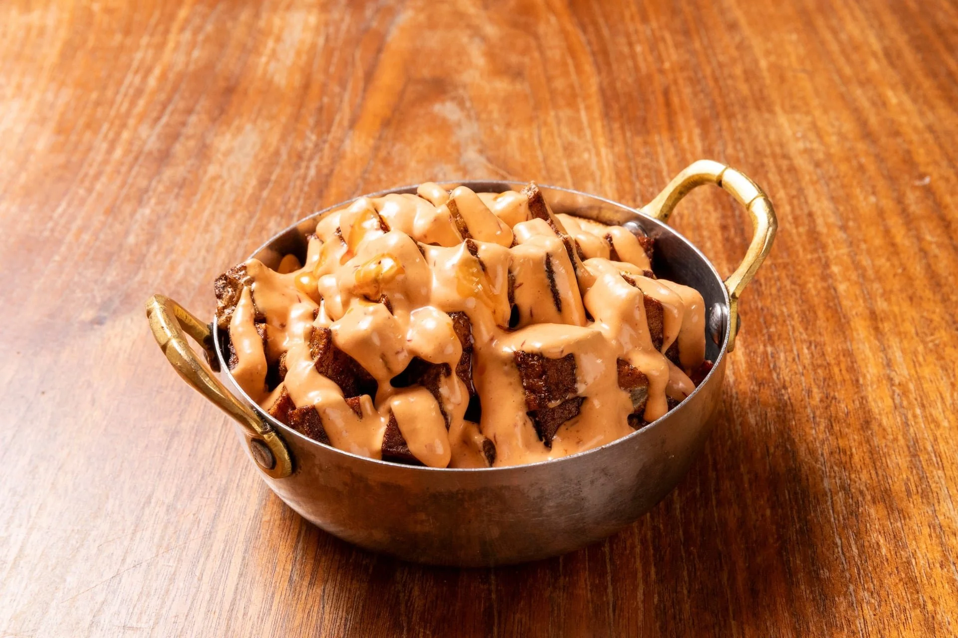A small metal serving dish with gold handles filled with waffles covered in peanut butter and topped with caramel syrup on a wooden table.