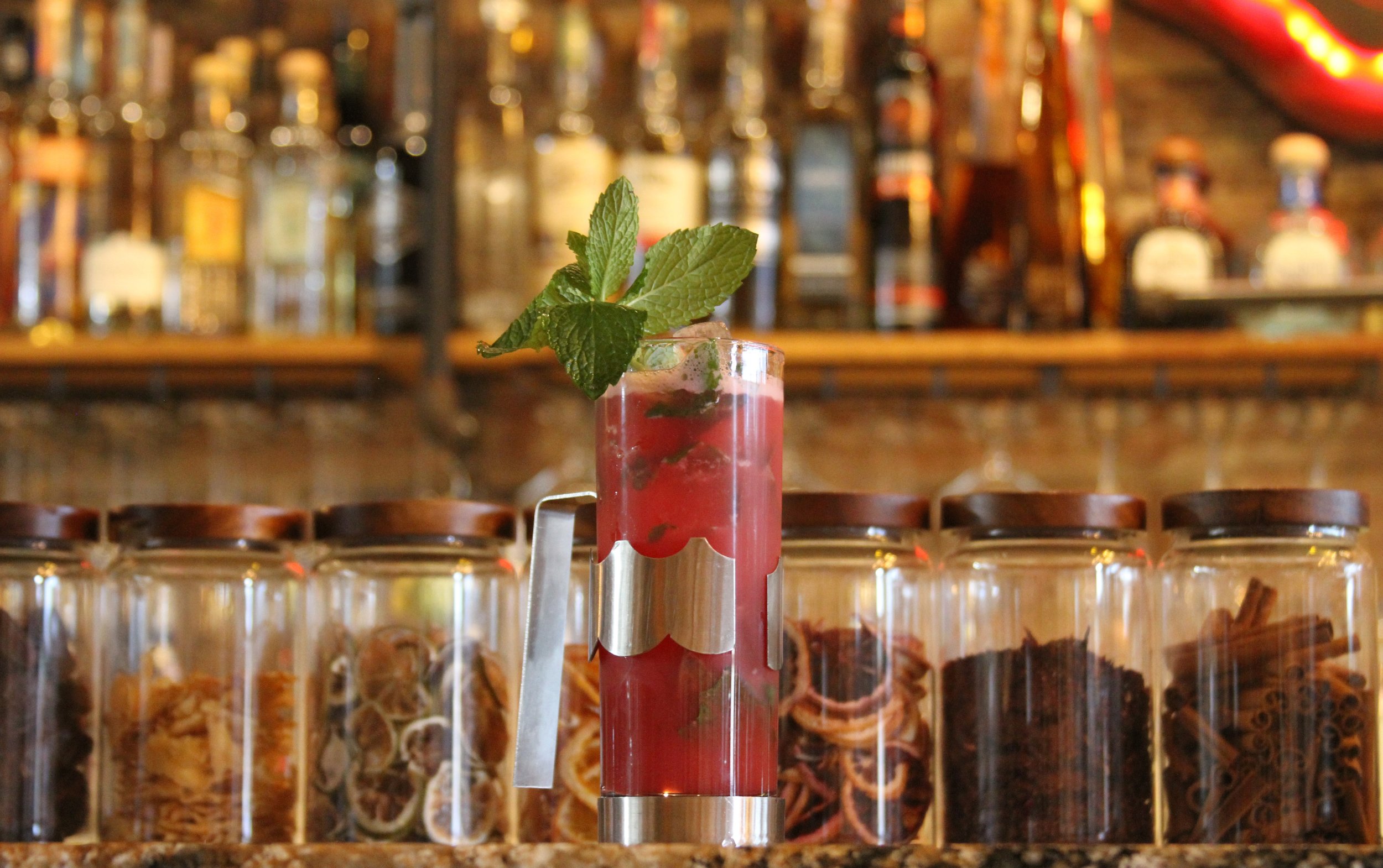 A drink garnished with fresh mint leaves on a bar counter with a blurred background of liquor bottles and bar decor.
