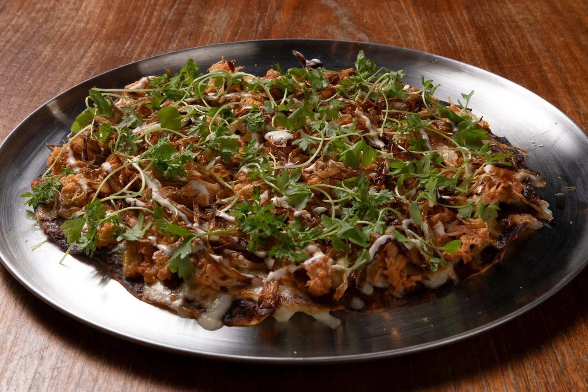 Pizza topped with shredded chicken, shredded cheese, fresh green herbs, and drizzled with white sauce on a metal tray.