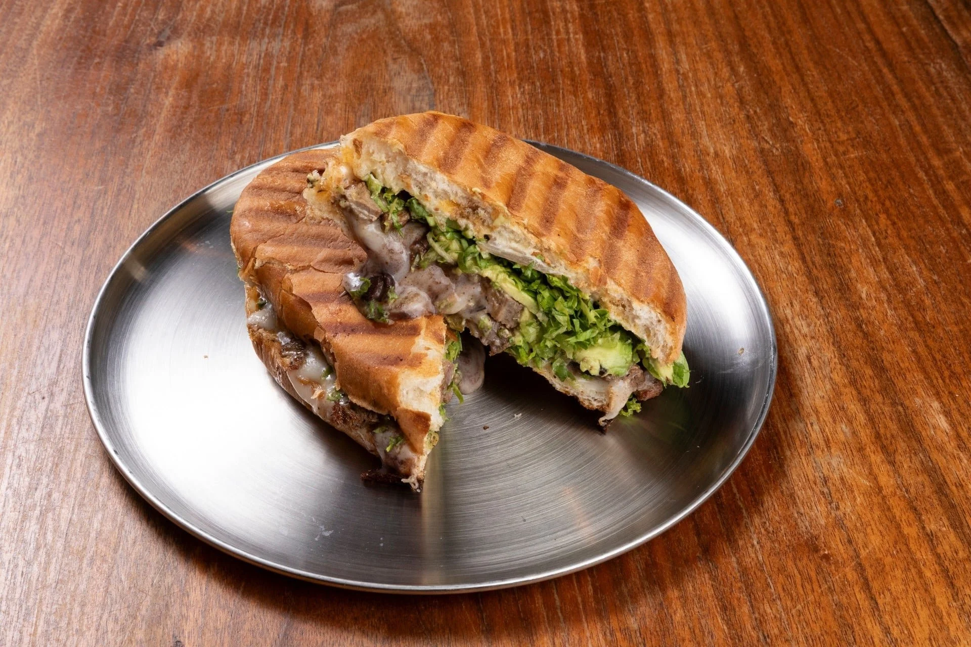 Cross-section of a grilled sandwich with lettuce, melted cheese, and beef on a metal tray, placed on a wooden table.