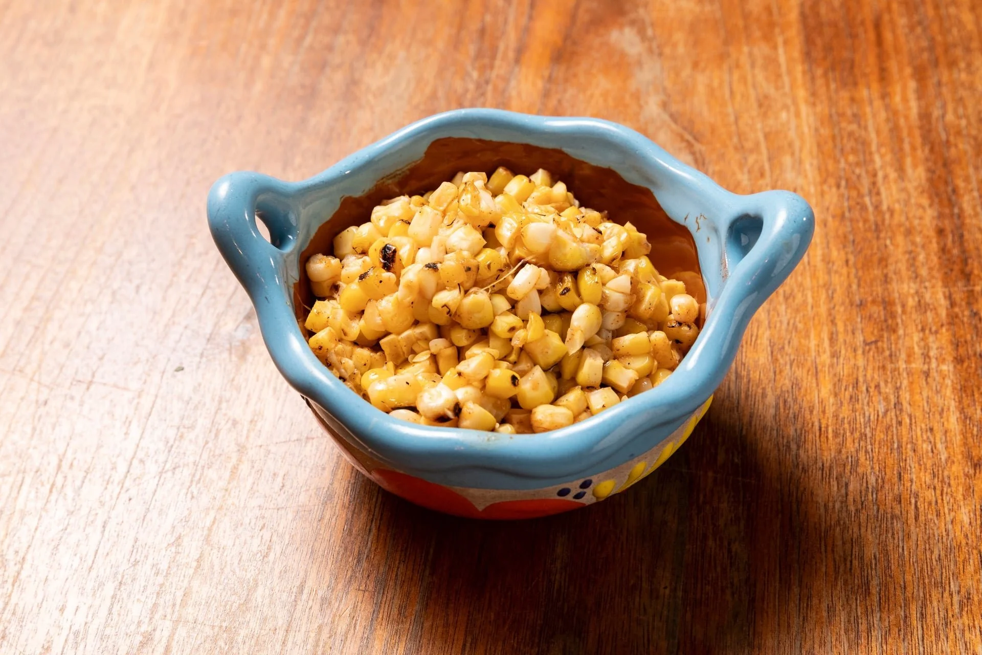 A small decorative bowl filled with charred grilled corn kernels on a wooden table.