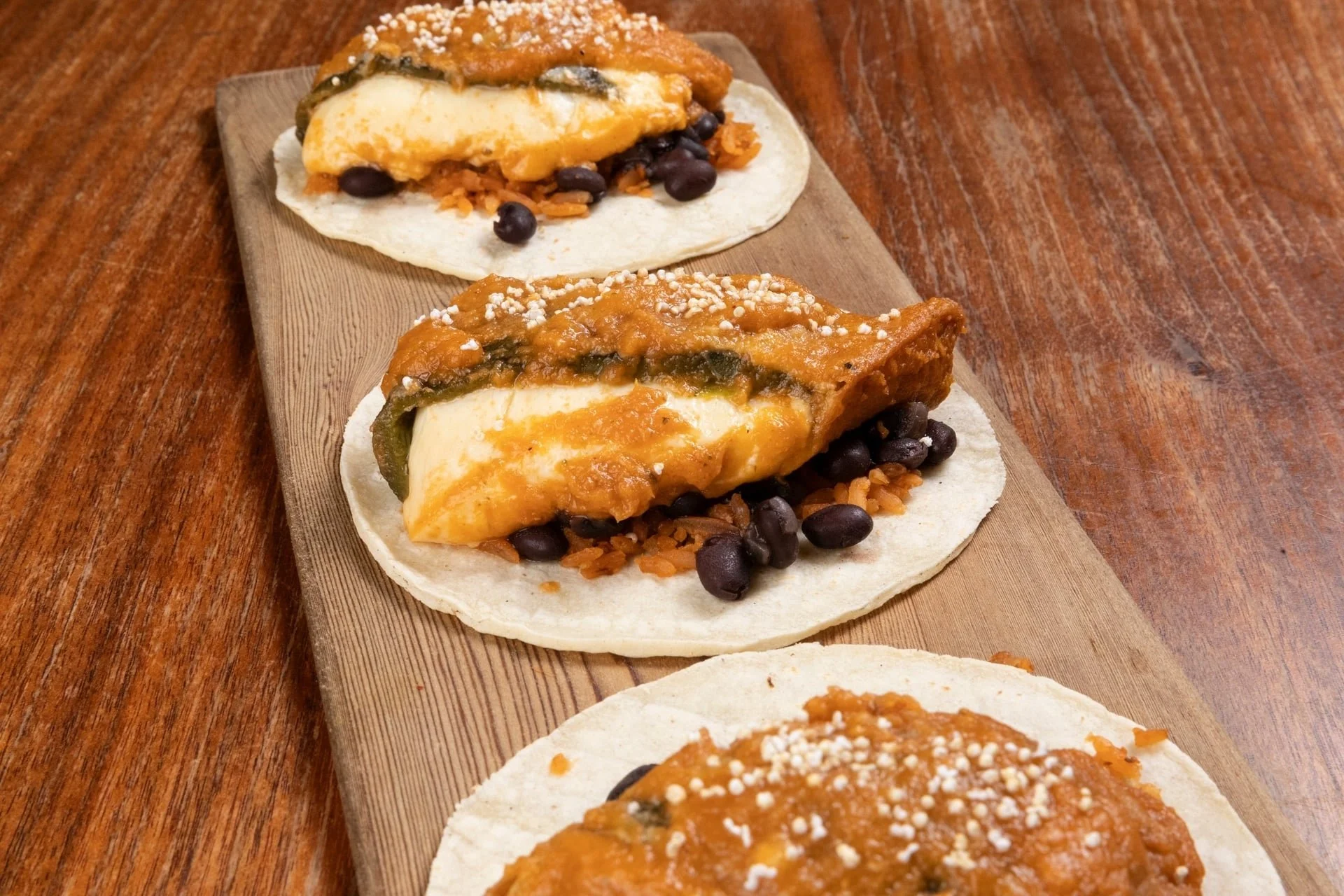 Two soft tacos filled with cheese, black beans, rice, and vegetables, served on a wooden platter.