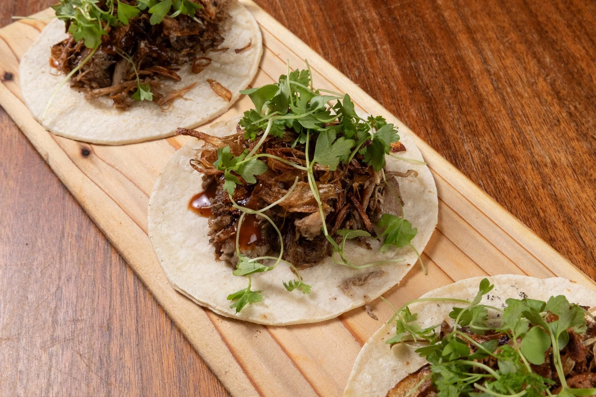 Close-up of shredded beef tacos topped with fresh cilantro on soft corn tortillas, served on a wooden platter.