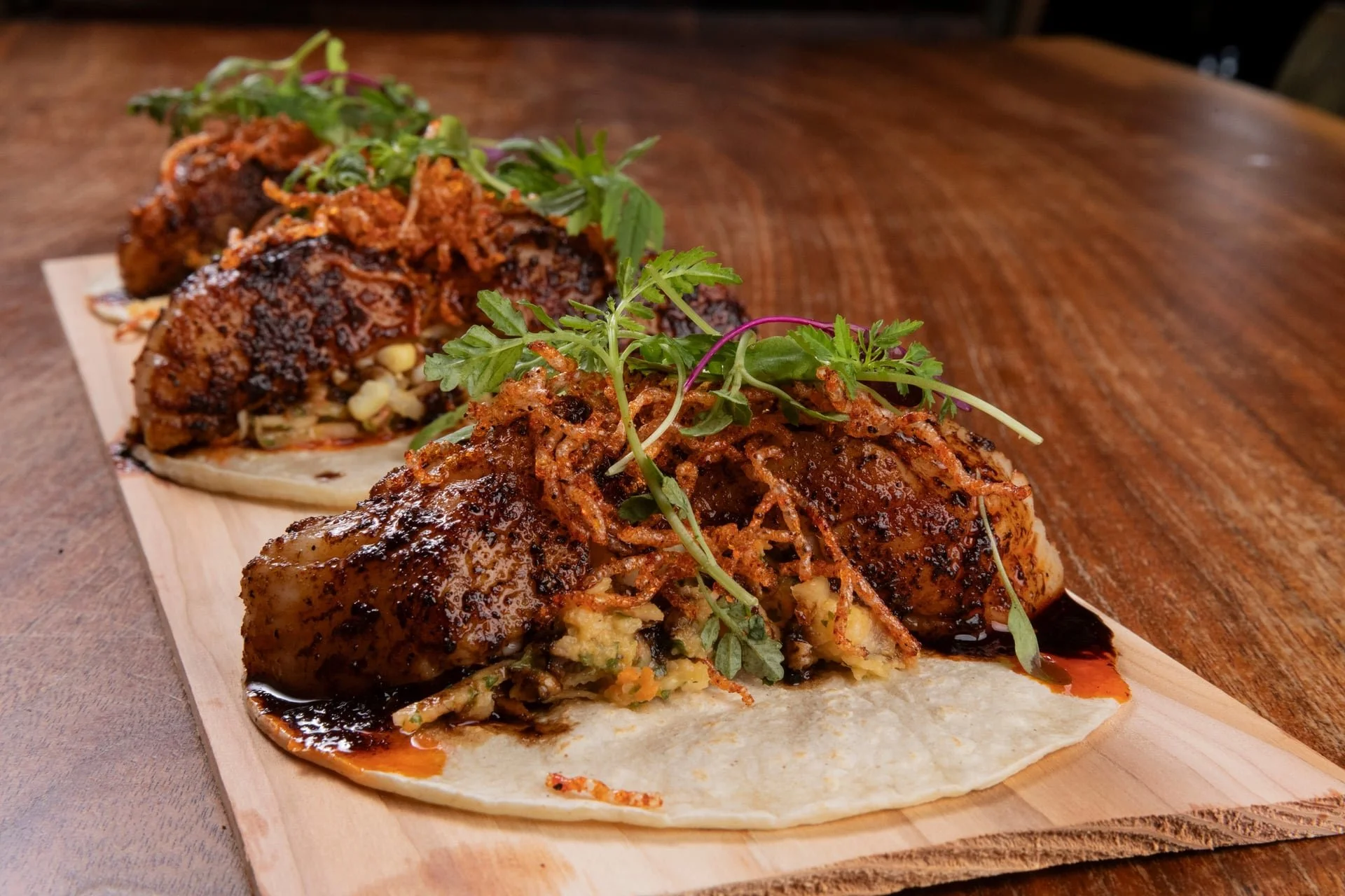 Close-up of gourmet tacos topped with microgreens, served on a wooden board.