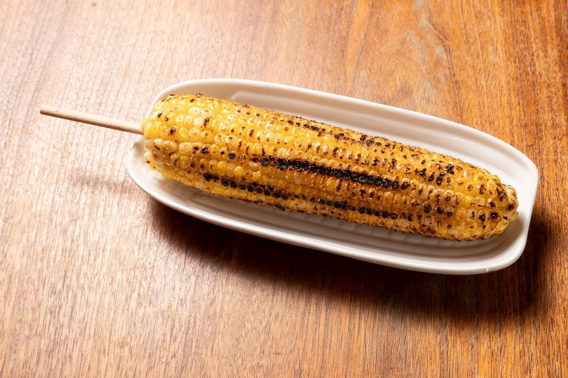 Grilled corn on the cob on a white plate on a wooden table.