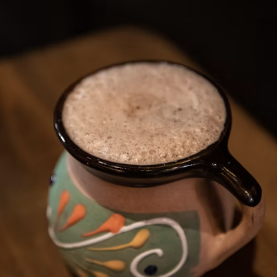 A ceramic coffee mug with colorful floral patterns filled with frothy coffee, placed on a wooden surface.