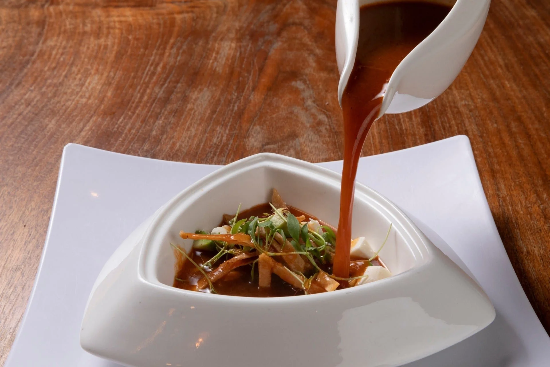 Pouring brown gravy over a bowl of salad with greens and vegetables on a white plate