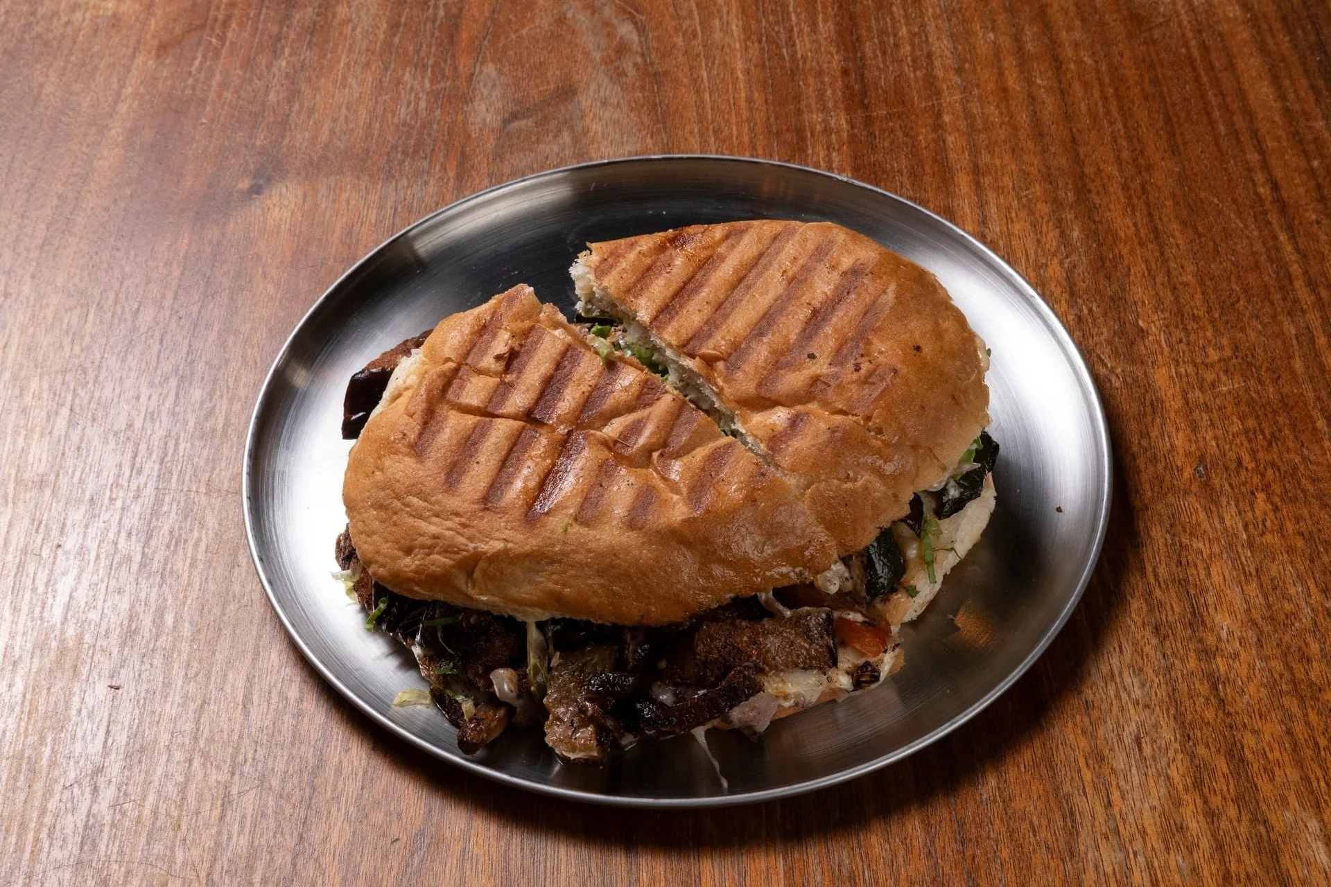 Grilled sandwich on a metal plate on a wooden table.