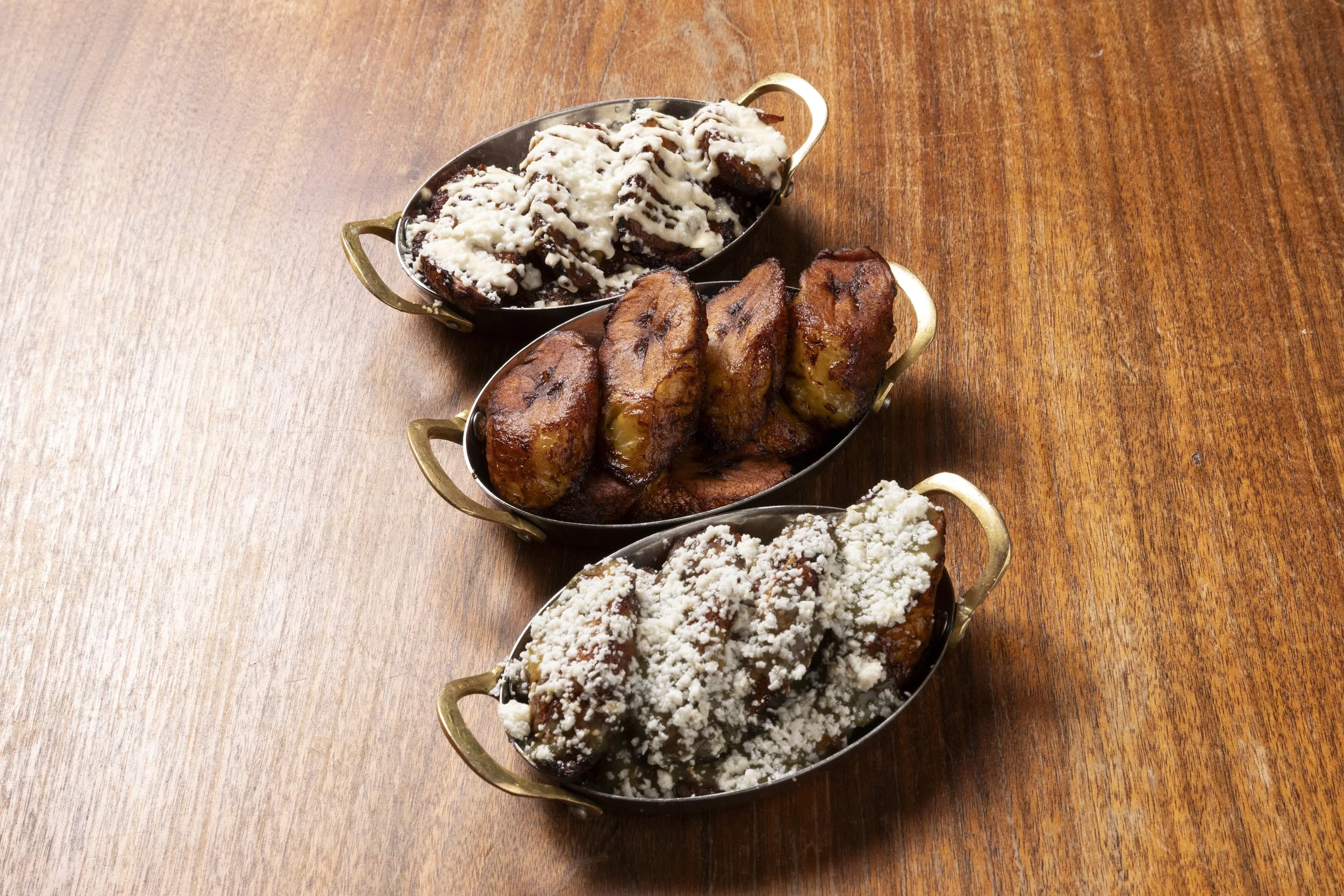 Three small serving dishes containing different desserts on a wooden table.