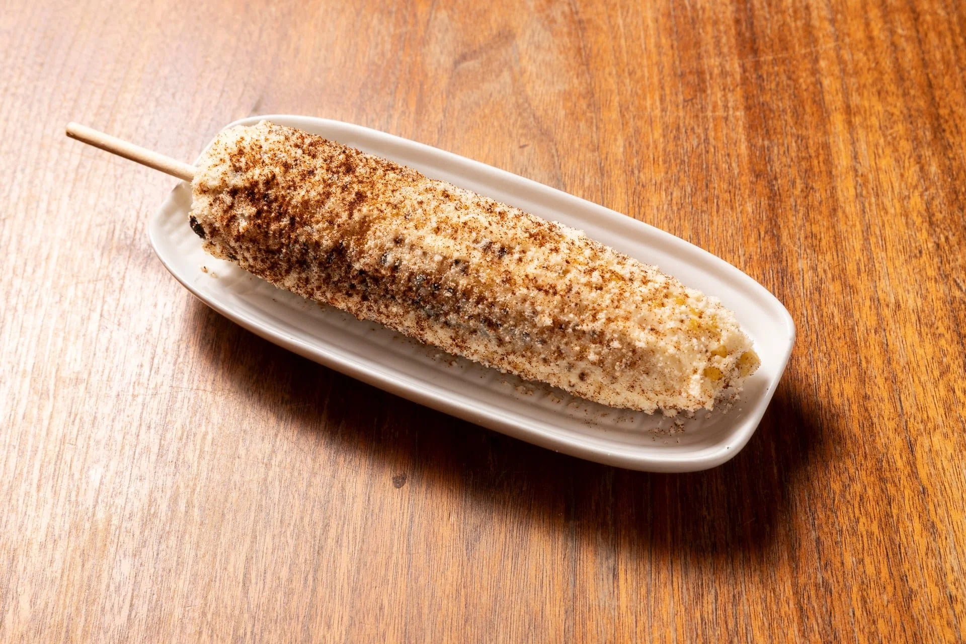 Ice cream bar on a stick coated with crushed nuts and chocolate powder, served on a white dish.