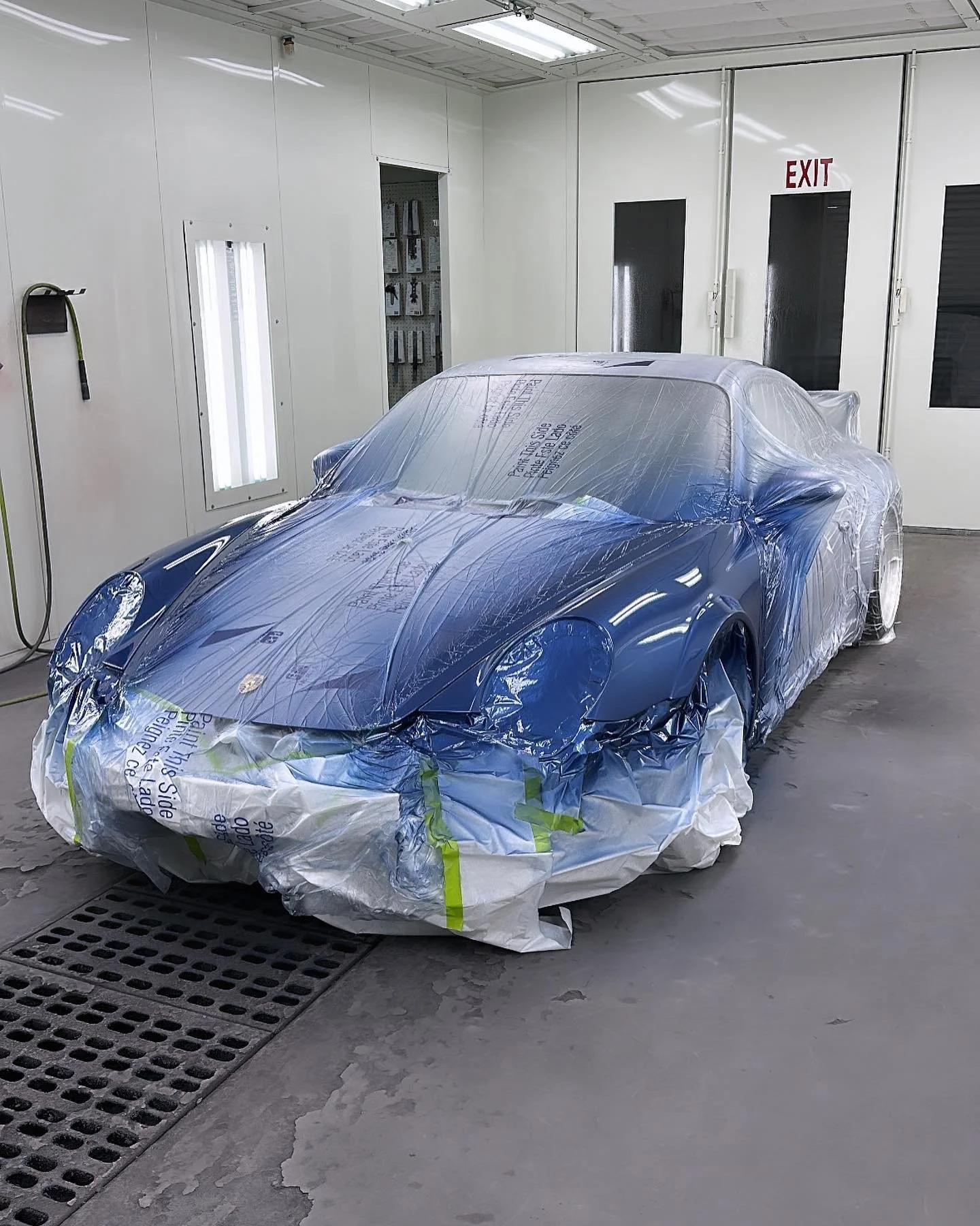 A blue sports car covered with protective plastic in a spray booth for painting or detailing.
