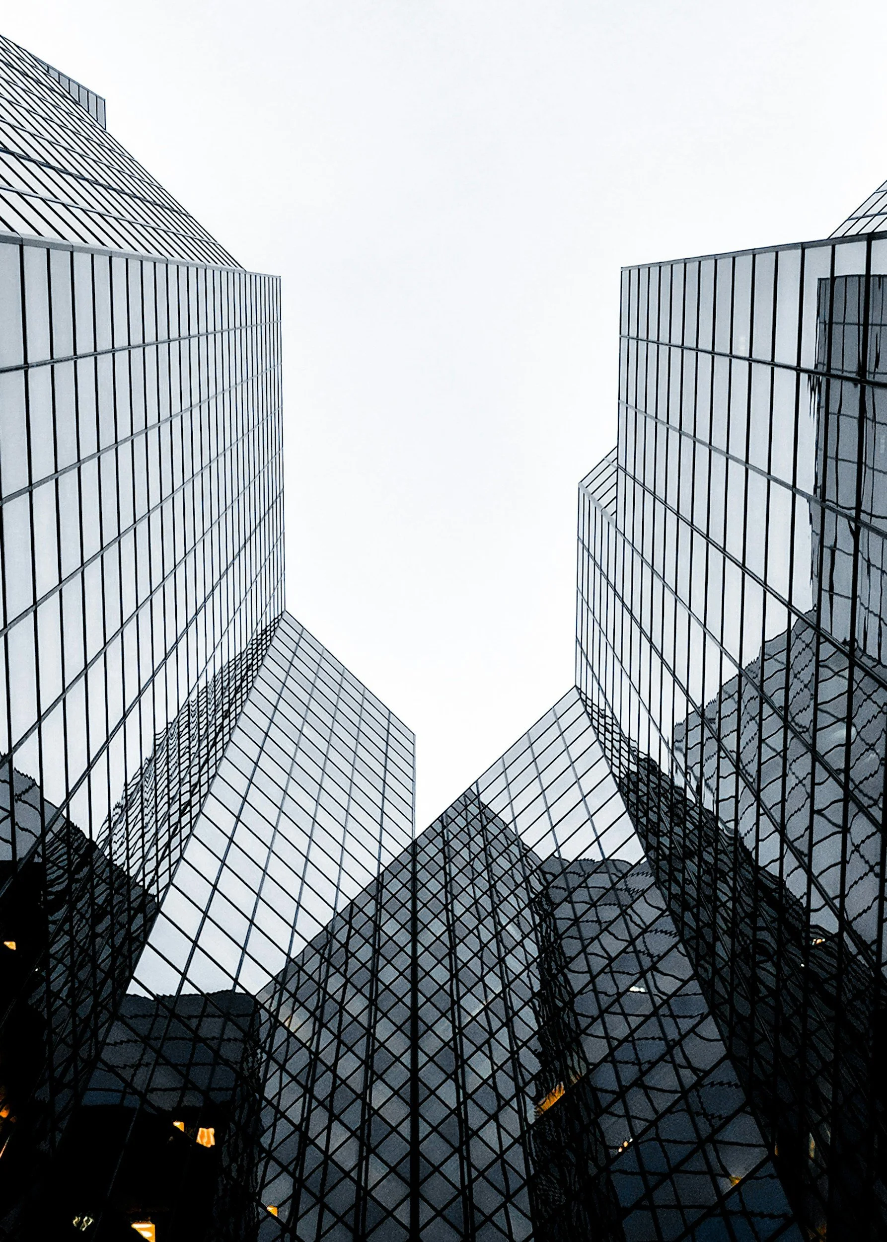 Looking up at tall, modern glass skyscrapers with reflective windows in an urban area.