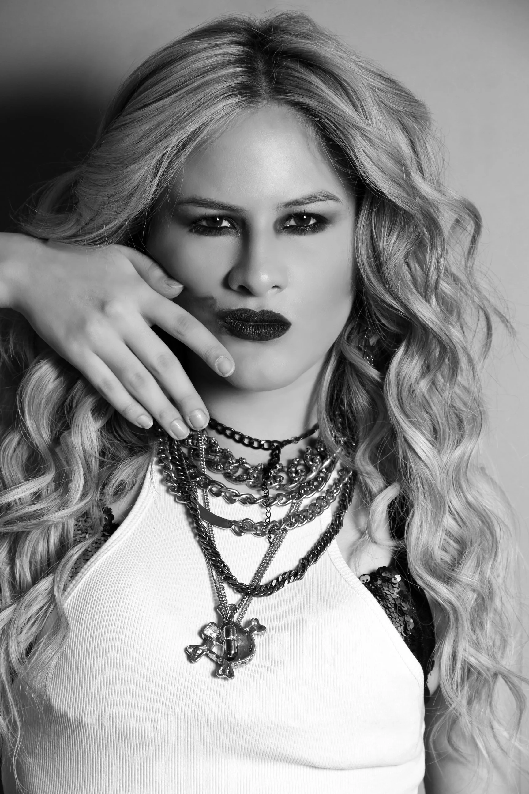 Retrato en blanco y negro de una mujer con cabello rizado y largo, vestida con un top de rayas blancas, usando múltiples collares y con el cabello peinado de manera suelta.