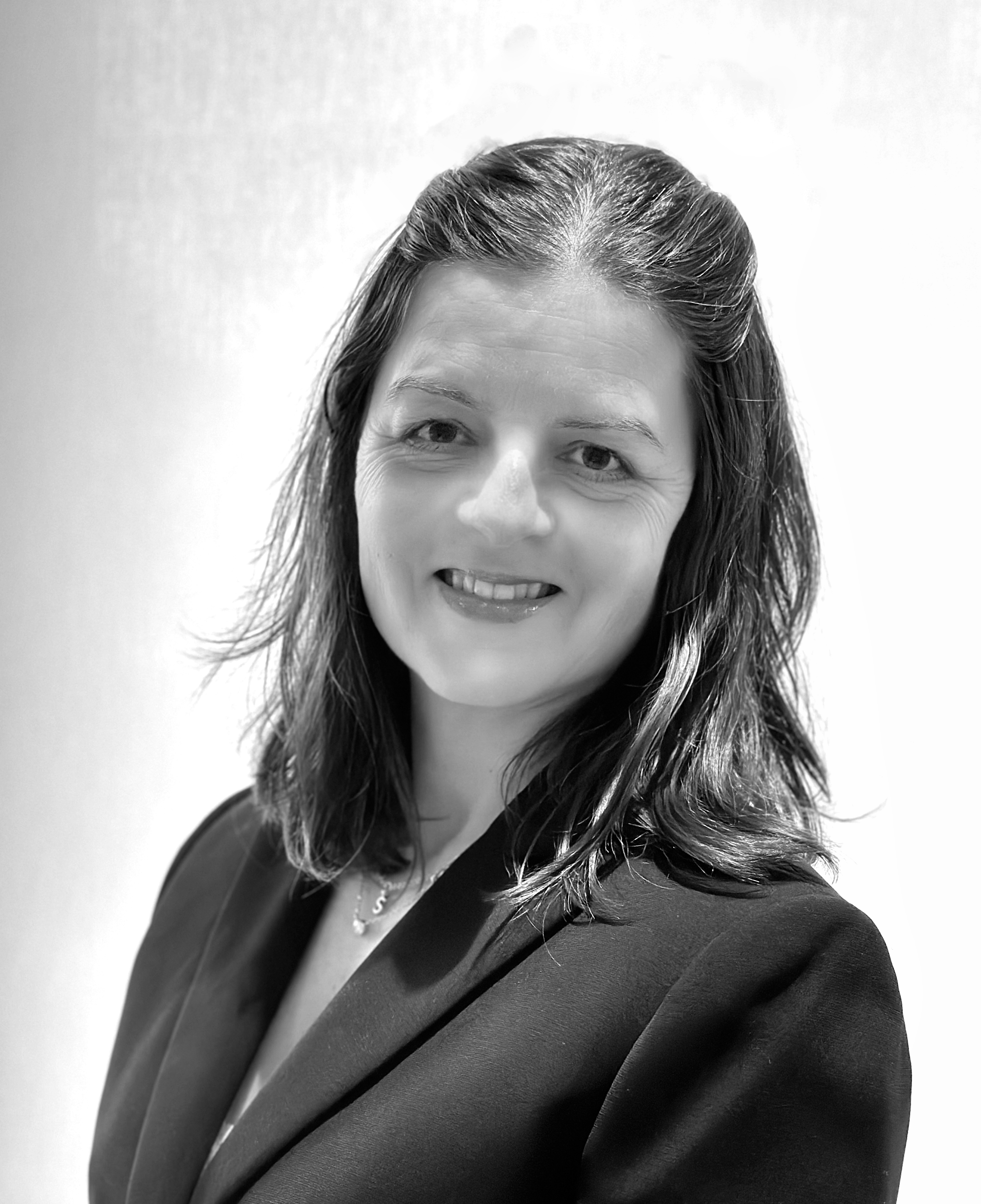 A black and white photograph of Suzanna Crescenzo smiling, with shoulder-length hair and wearing a dark top.